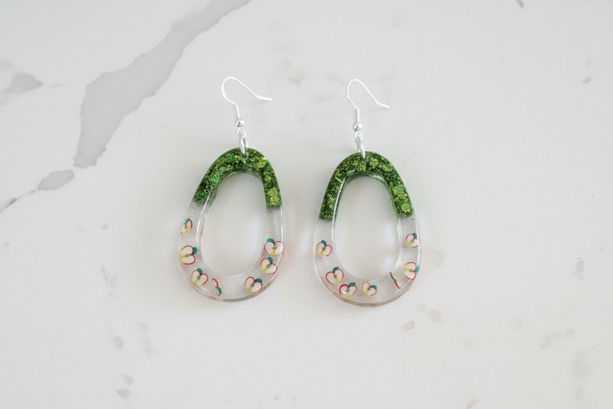 Green earrings with apple patterns on a light gray background