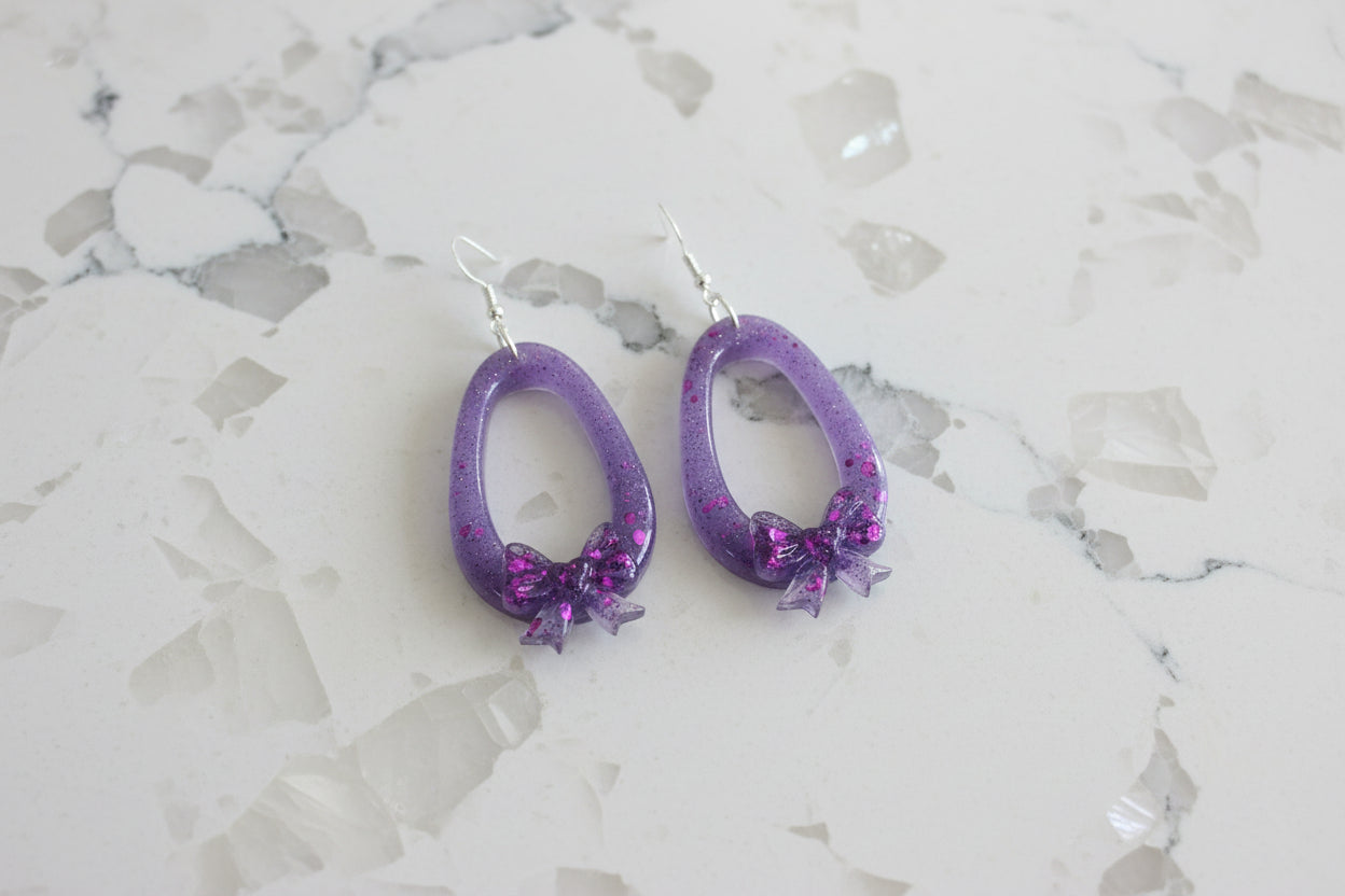 Purple hoop earrings with bow details on a marble surface