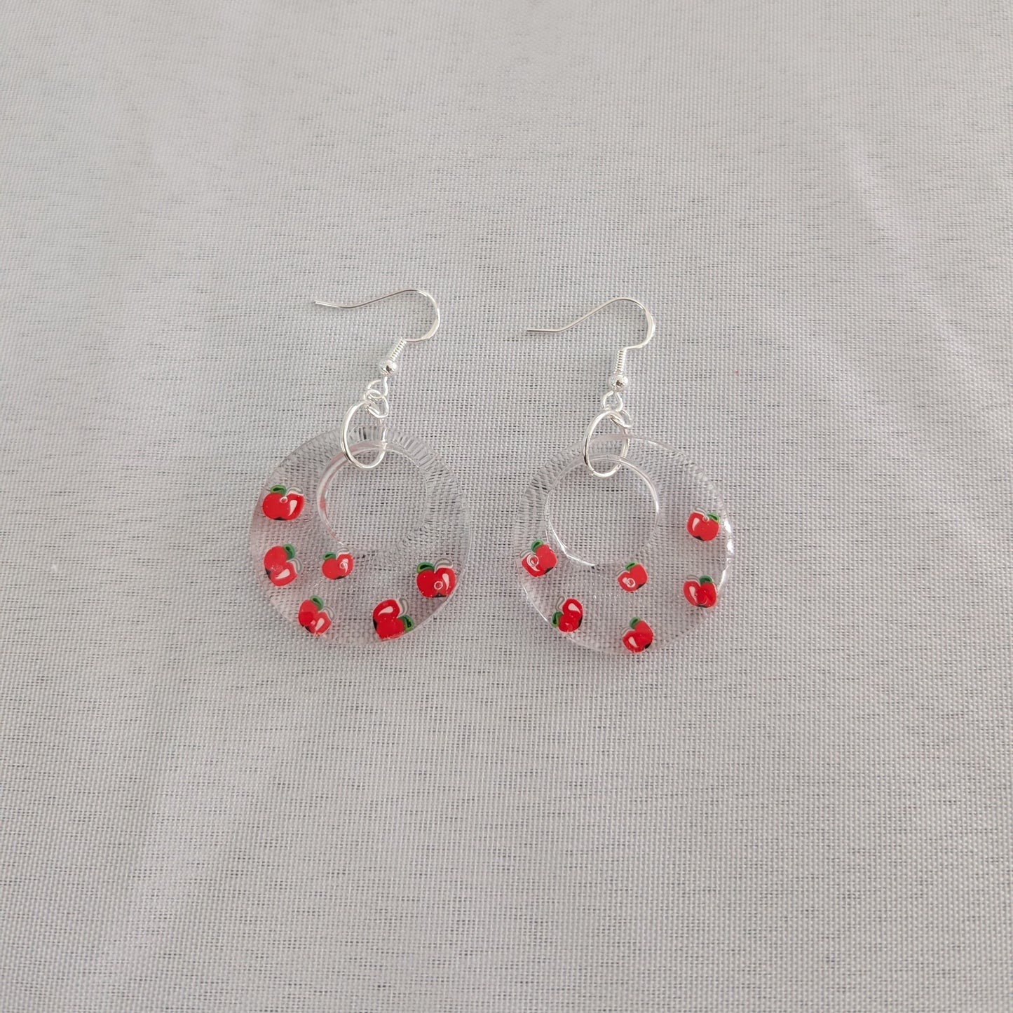 Hoop earrings with red apple accents on a gray background