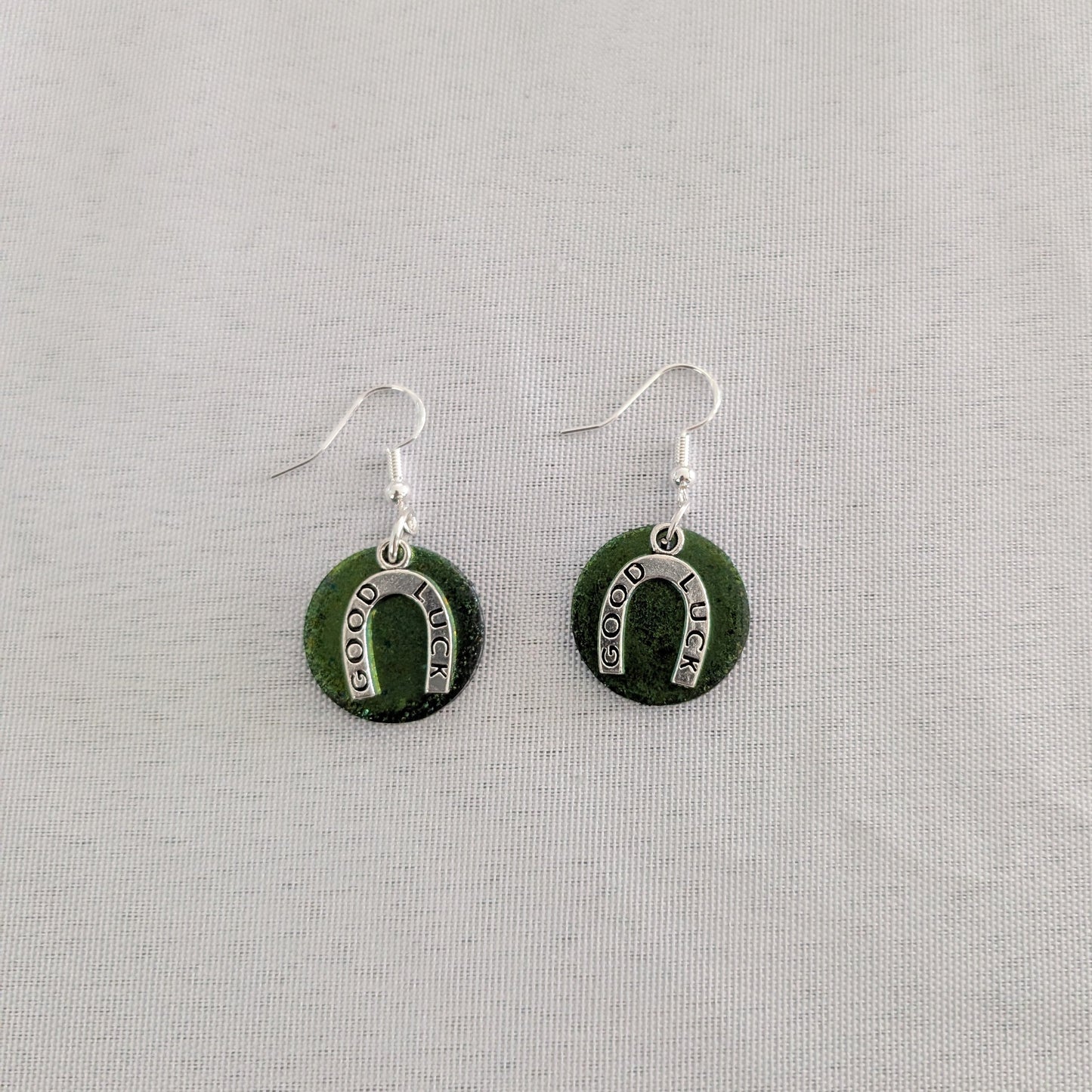 Green circular earrings with silver horseshoe design on a light gray background