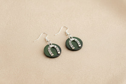 Pair of green earrings with silver horseshoe designs on a beige background