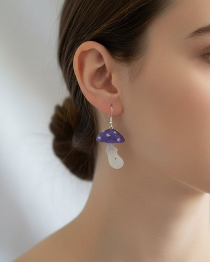 Mushroom-shaped earrings being worn by a person with a blurred background