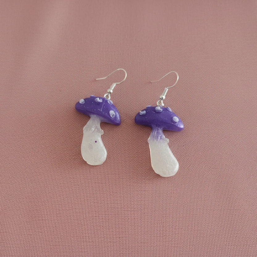 Purple and white mushroom-shaped earrings on a pink background