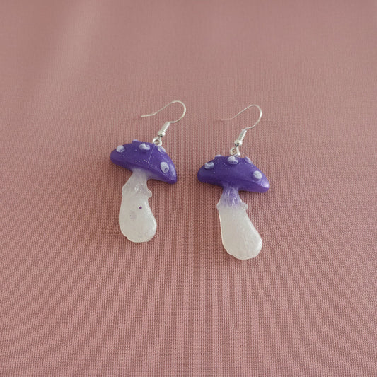 Purple and white mushroom-shaped earrings on a pink background