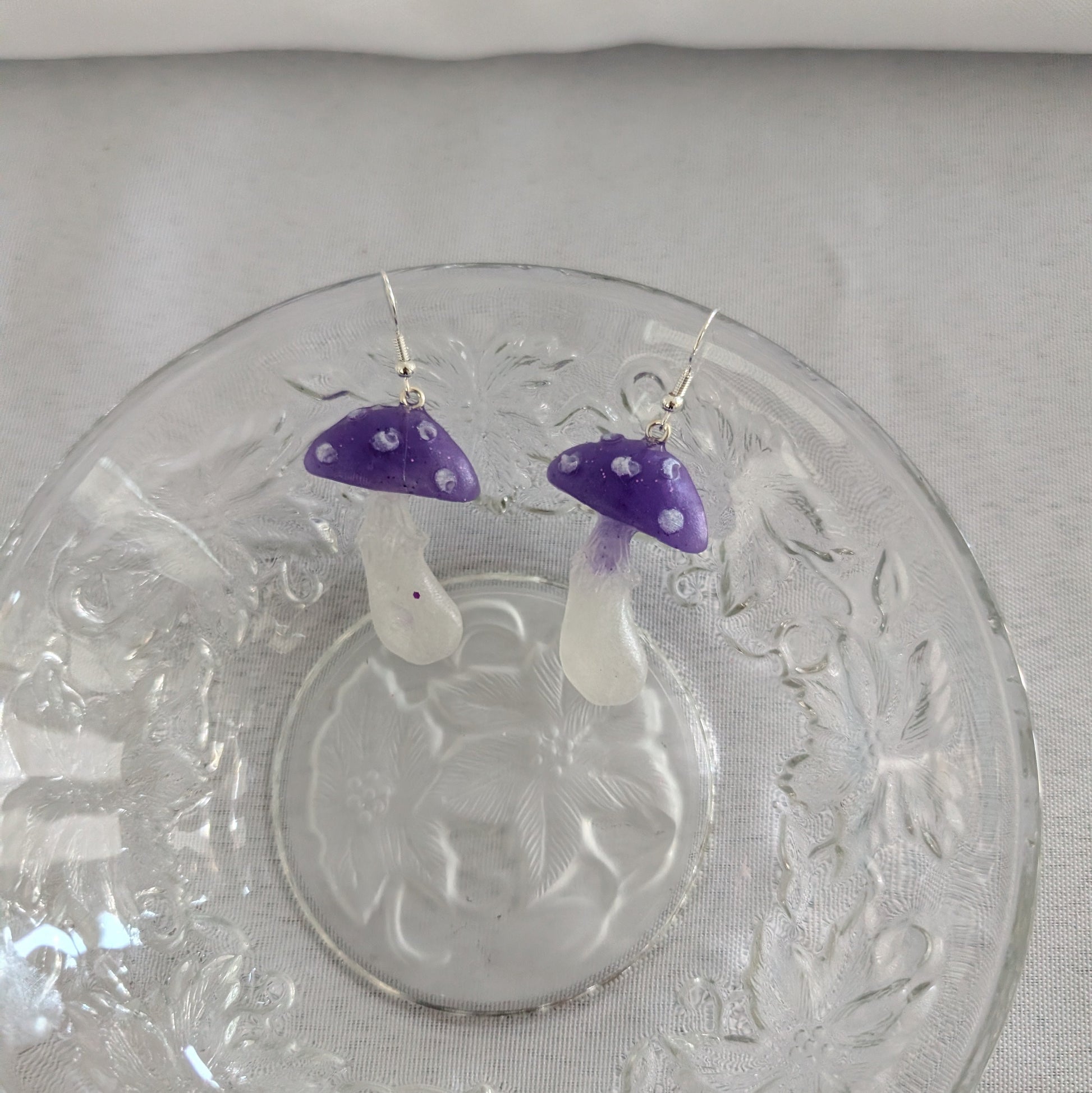 Mushroom-shaped earrings with purple caps on a decorative glass plate.