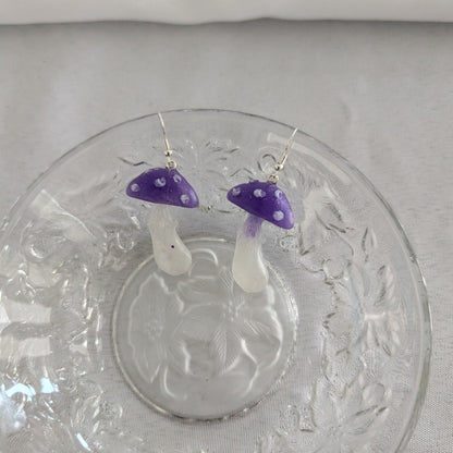 Mushroom-shaped earrings with purple caps on a decorative glass plate.
