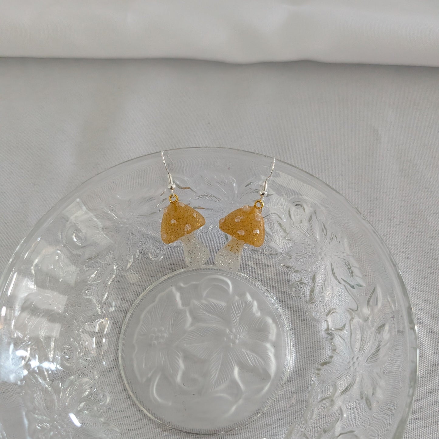 God mushroom-shaped earrings on a decorative glass plate with a white background