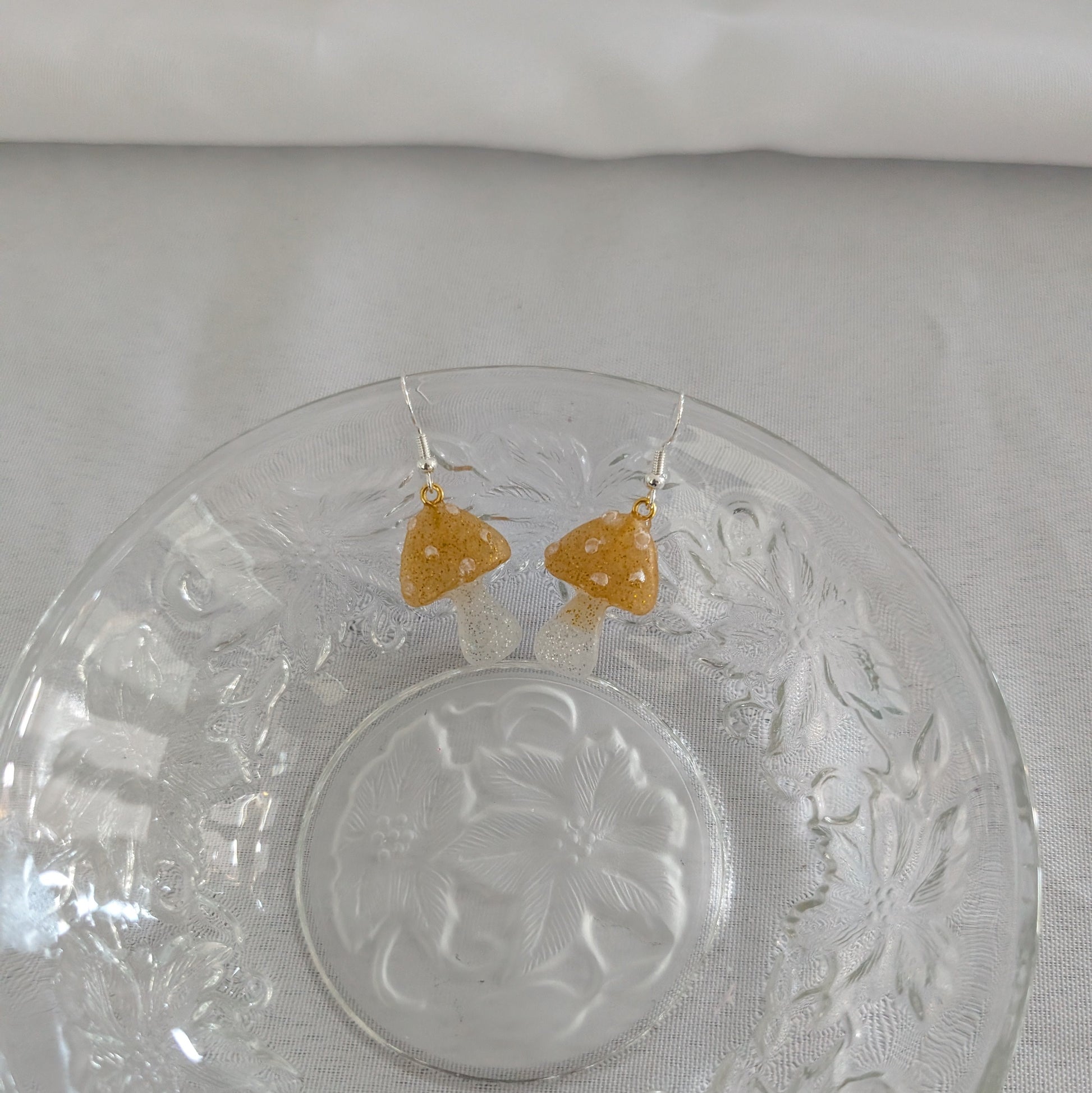 God mushroom-shaped earrings on a decorative glass plate with a white background