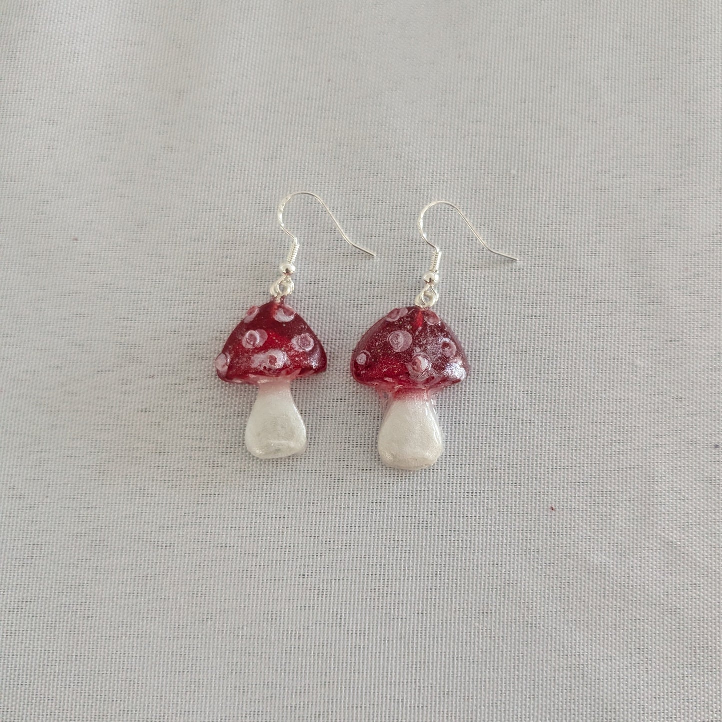 Mushroom-shaped earrings with red caps and white bases on a light gray background