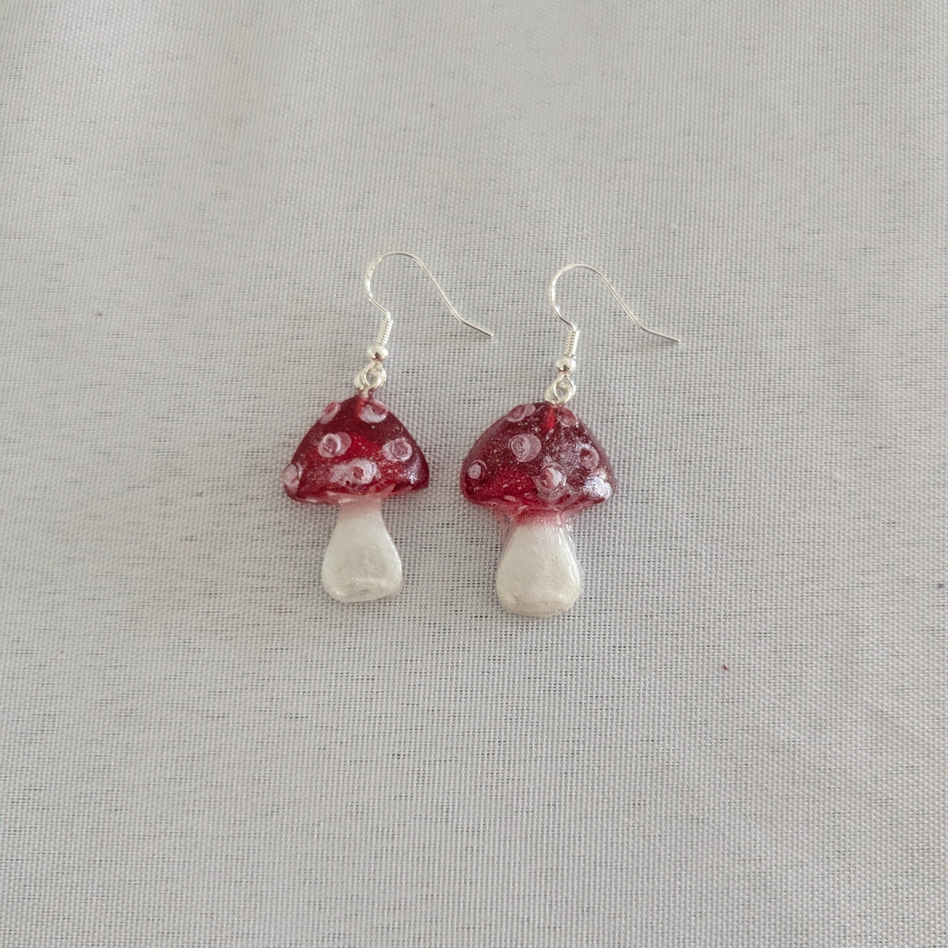 Mushroom-shaped earrings with red caps and white bases on a light gray background