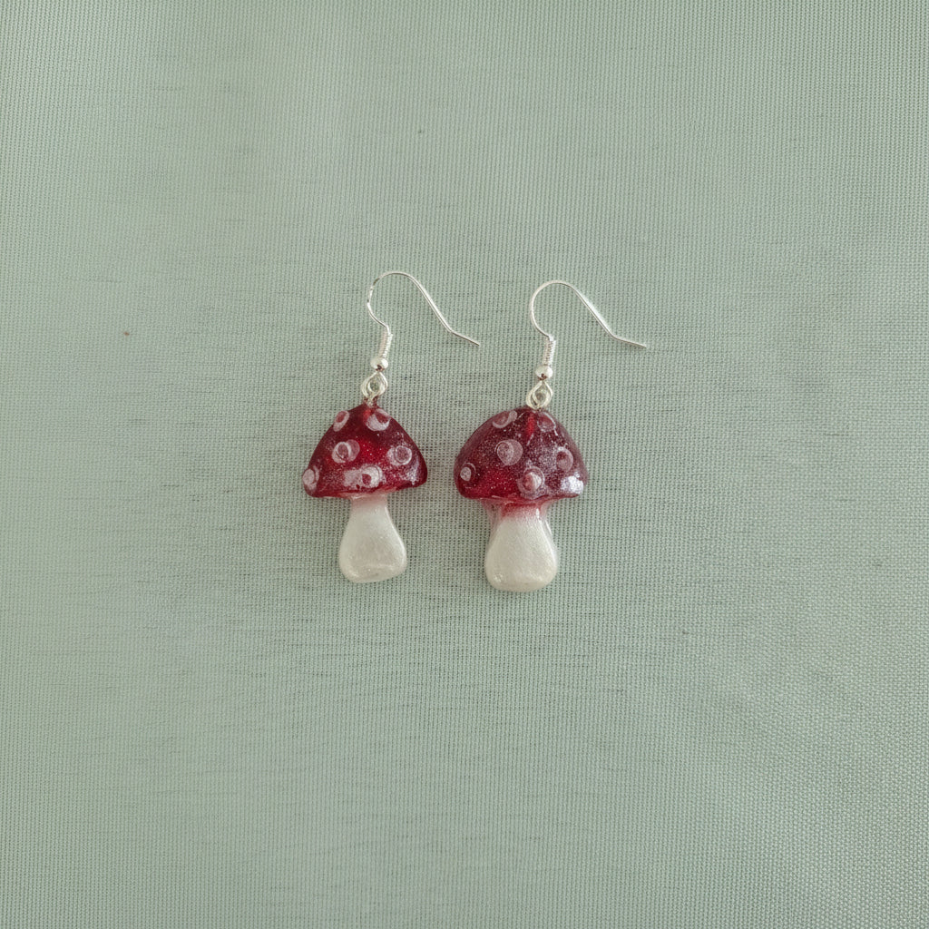 Mushroom-shaped earrings with red caps and white stems on a light green background