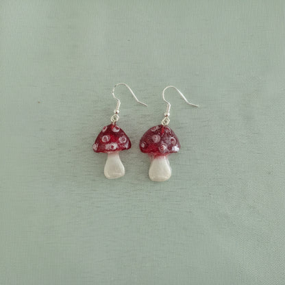 Mushroom-shaped earrings with red caps and white stems on a light green background