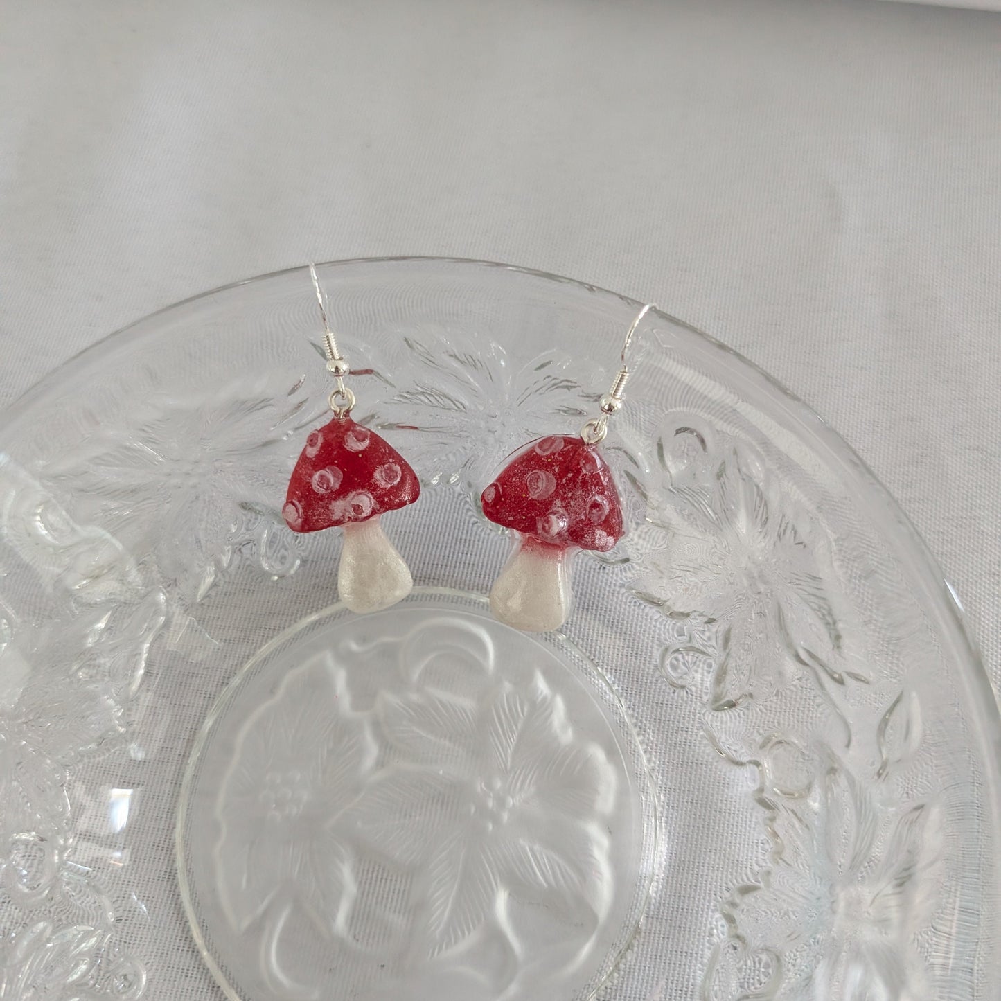 Red mushroom-shaped earrings on a clear glass plate with a white background