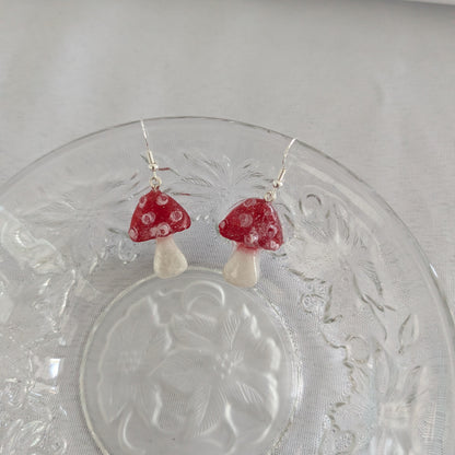 Red mushroom-shaped earrings on a clear glass plate with a white background