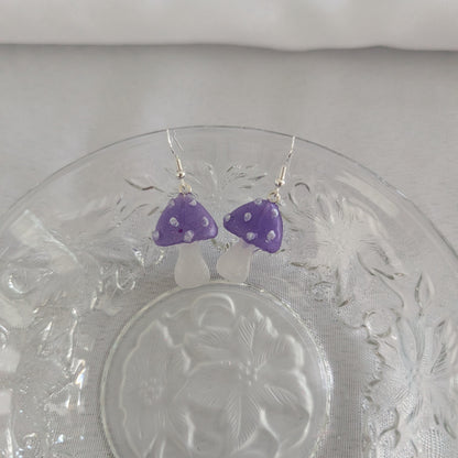 Purple mushroom-shaped earrings on a glass plate with a white background