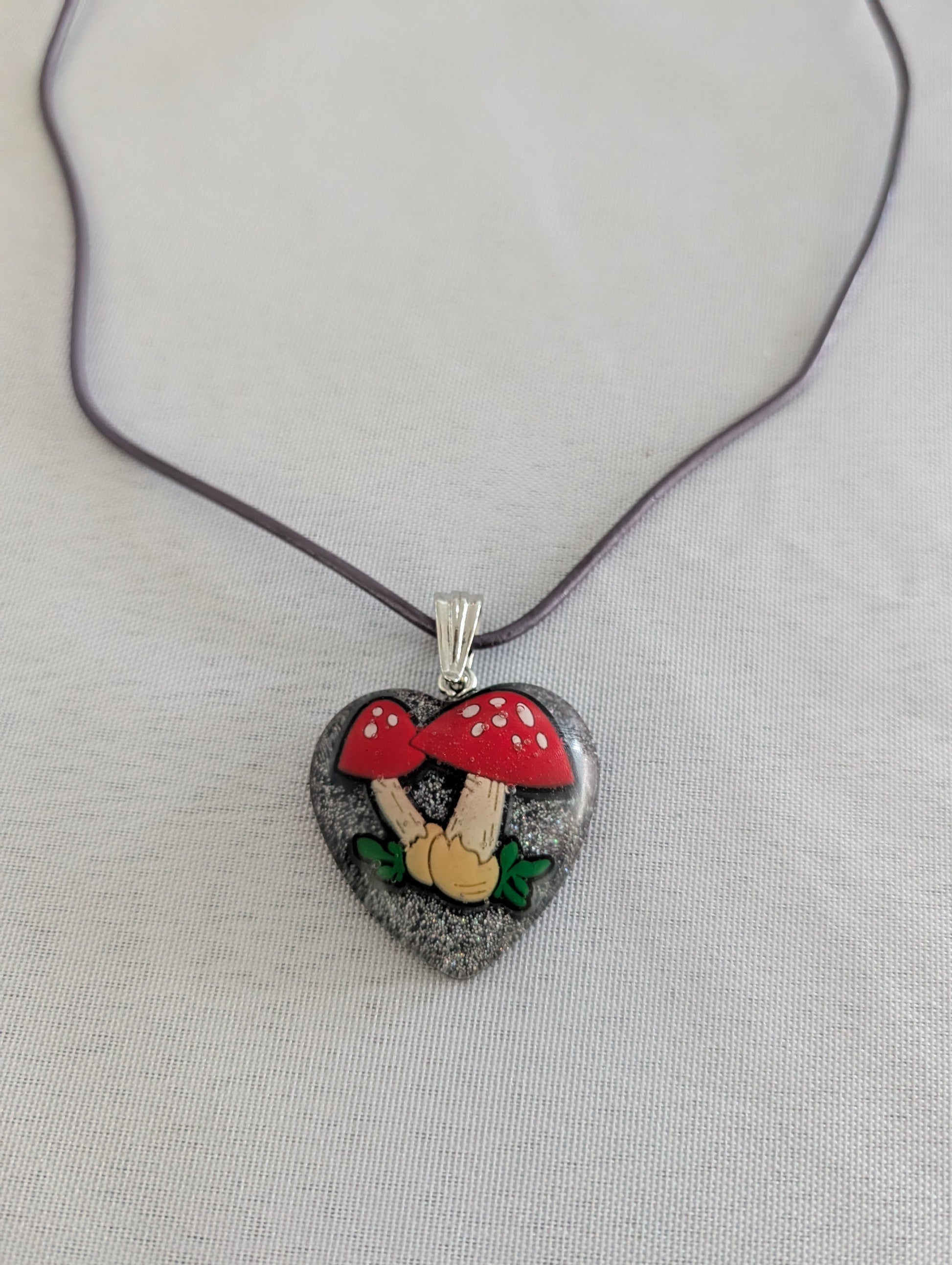 Heart-shaped pendant with mushroom design on a gray background