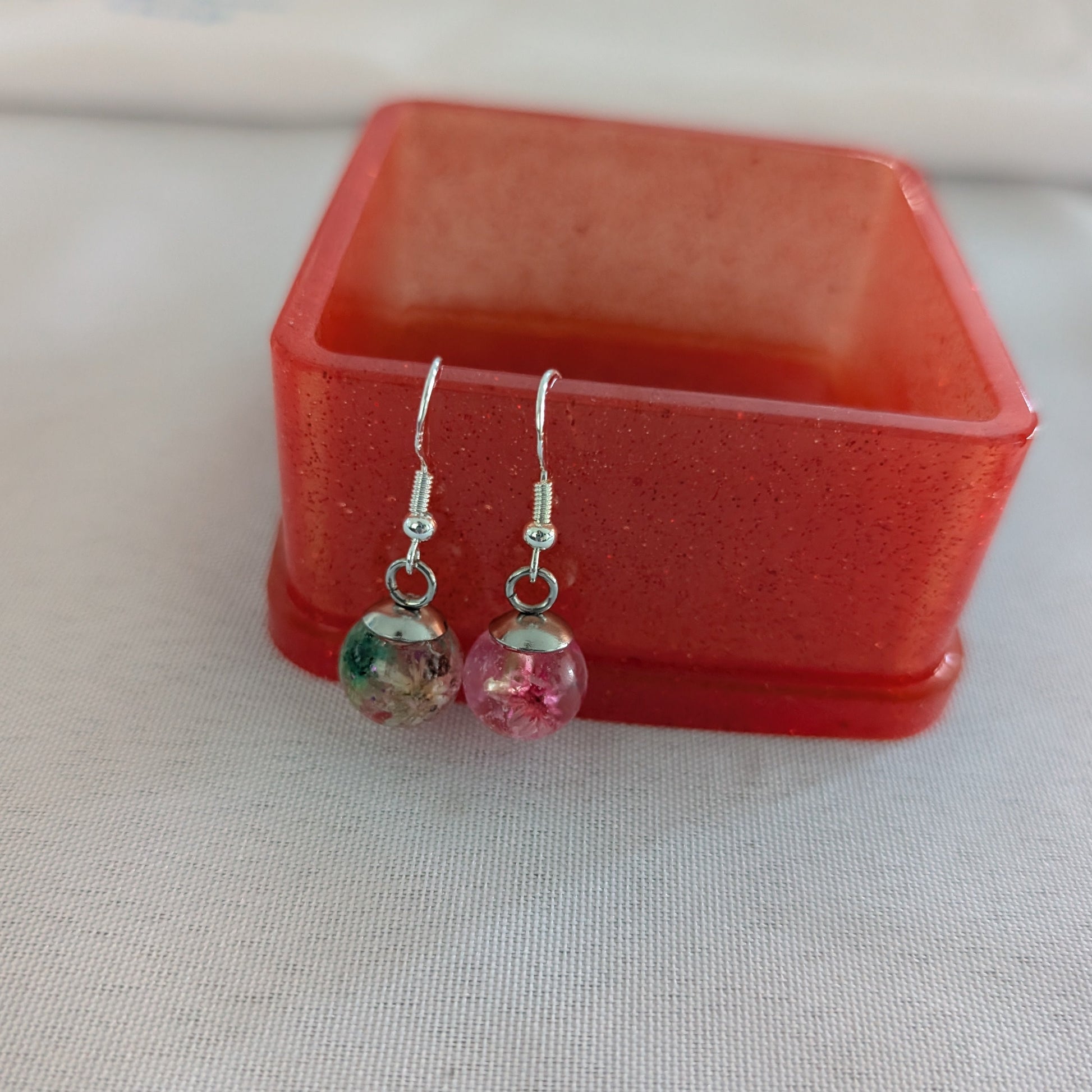 Pair of earrings with colorful beads in front of a red jewelry box on a light background