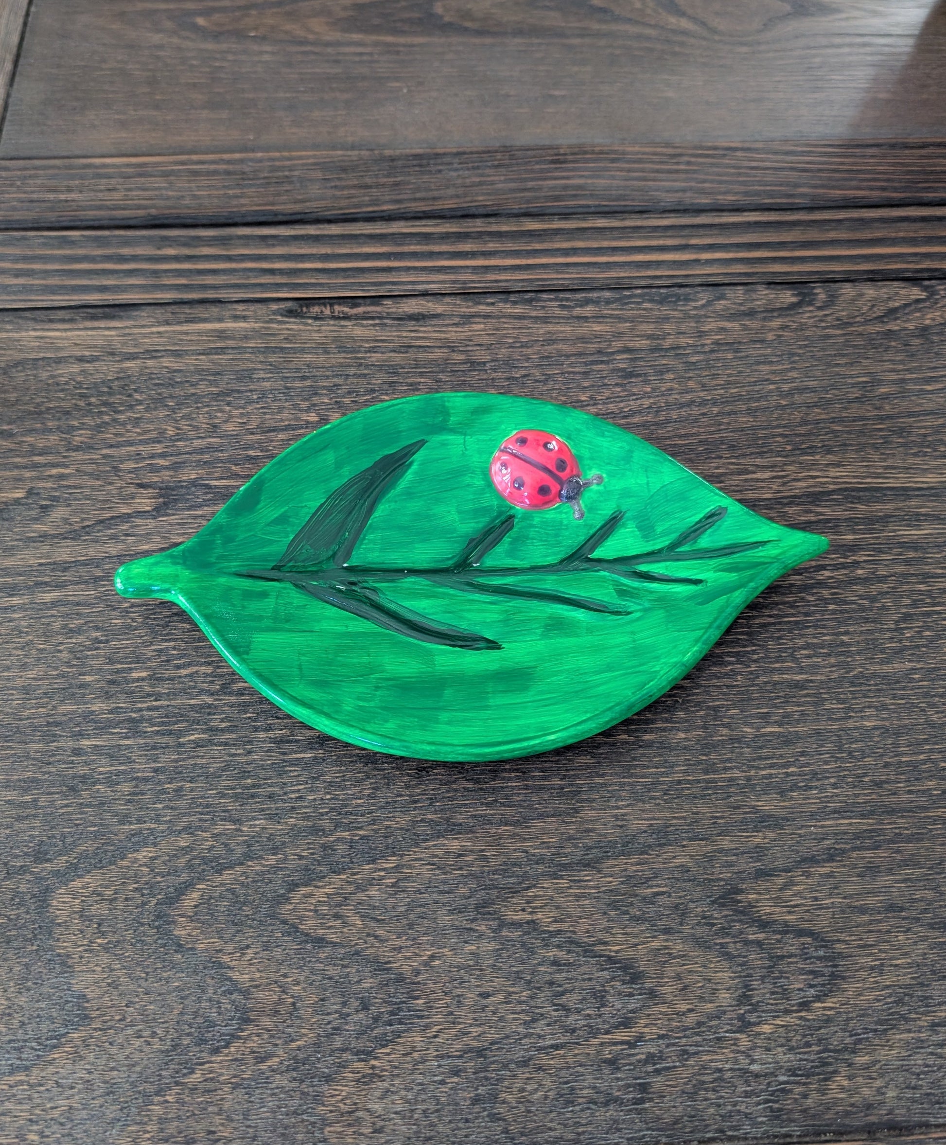 Green leaf-shaped object with a ladybug on a wooden surface