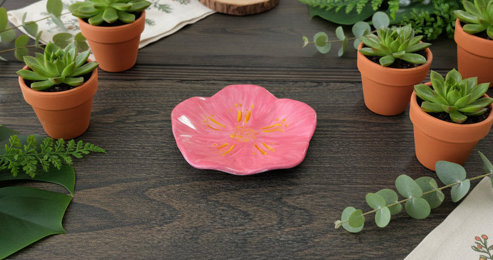 Pink flower-shaped dish on a wooden surface with potted plants