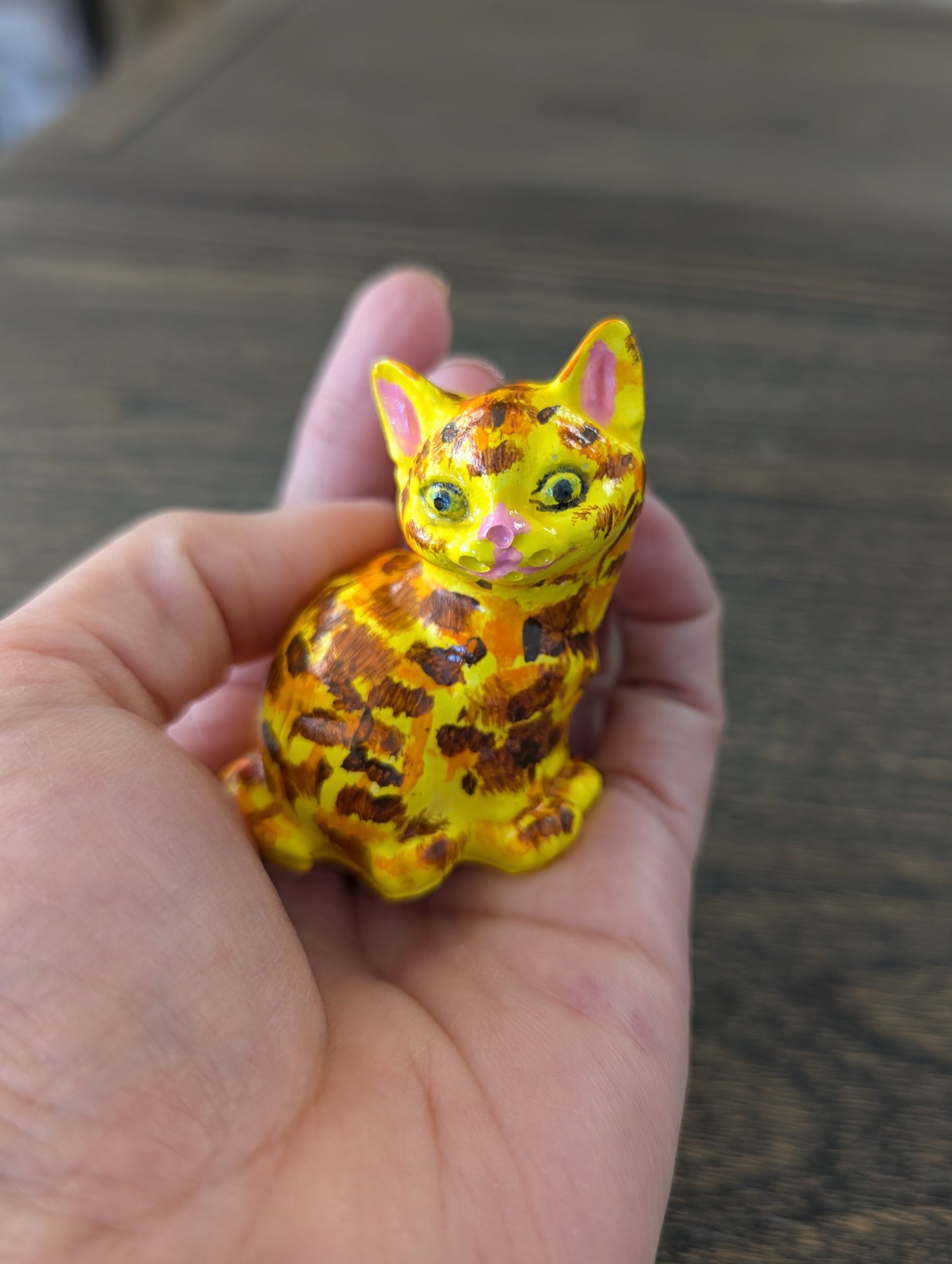 Small yellow cat figurine held in a hand against a wooden surface
