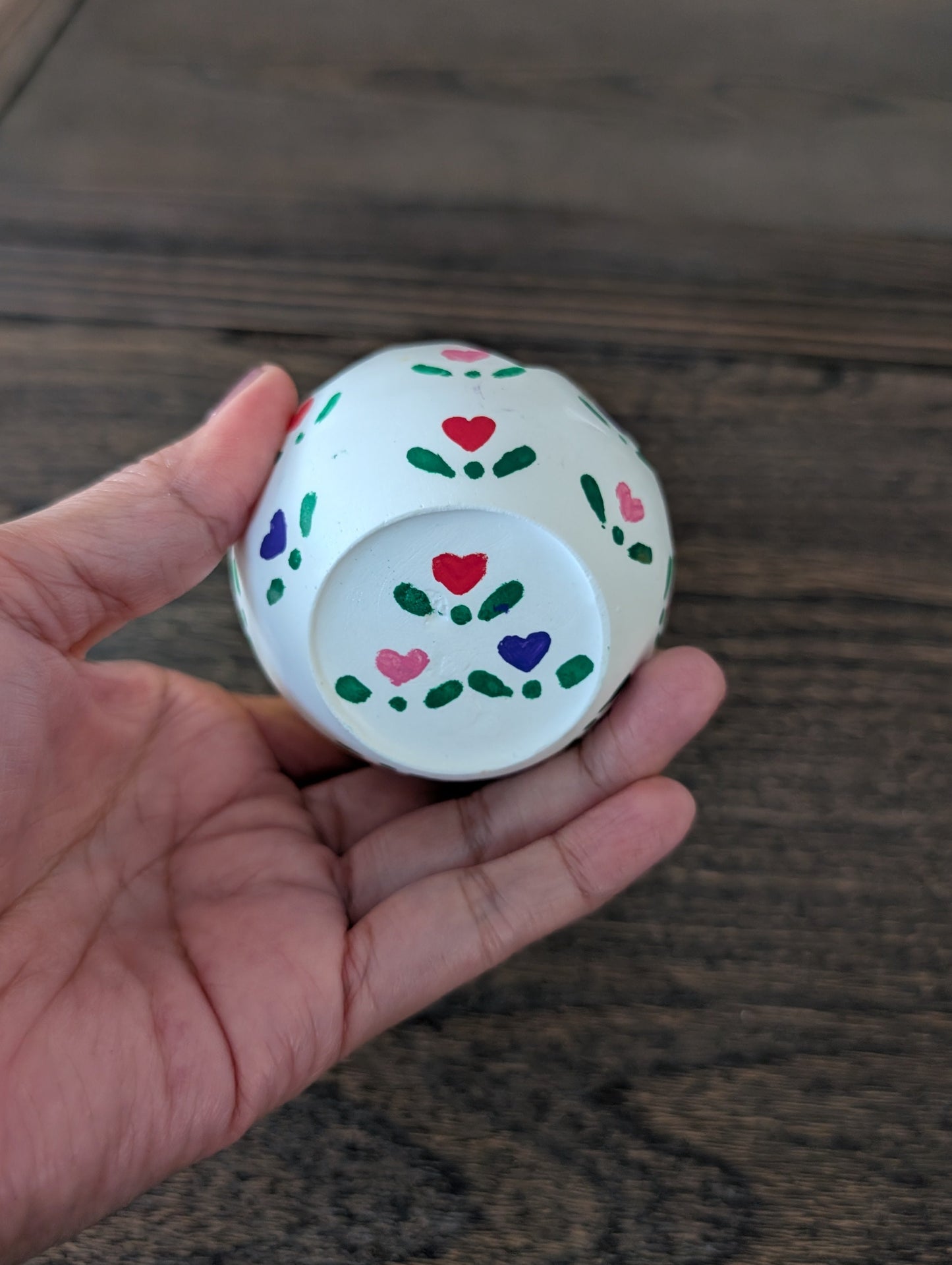 Small decorative object with heart patterns held in a hand on a wooden surface