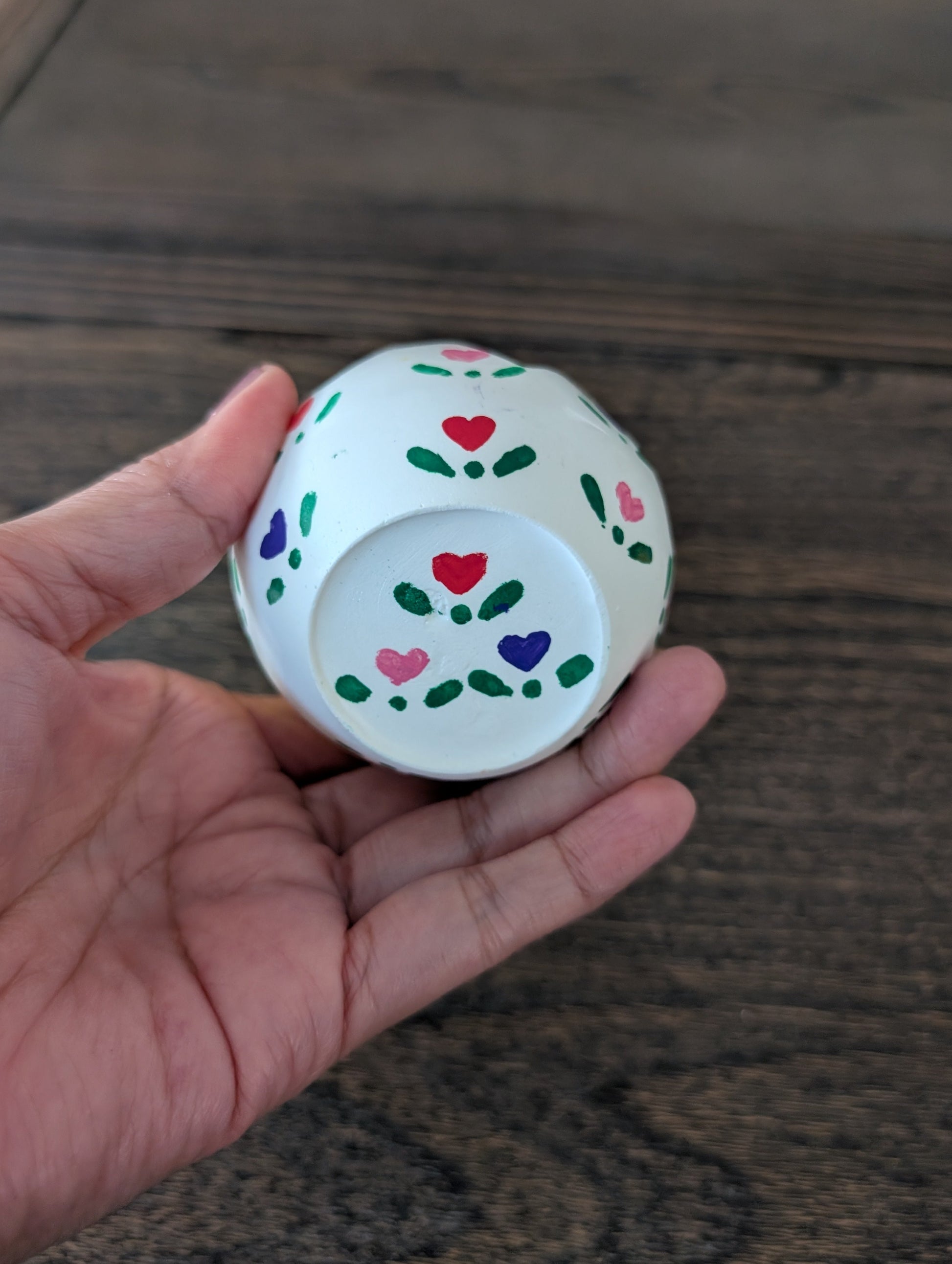 Small decorative object with heart patterns held in a hand on a wooden surface