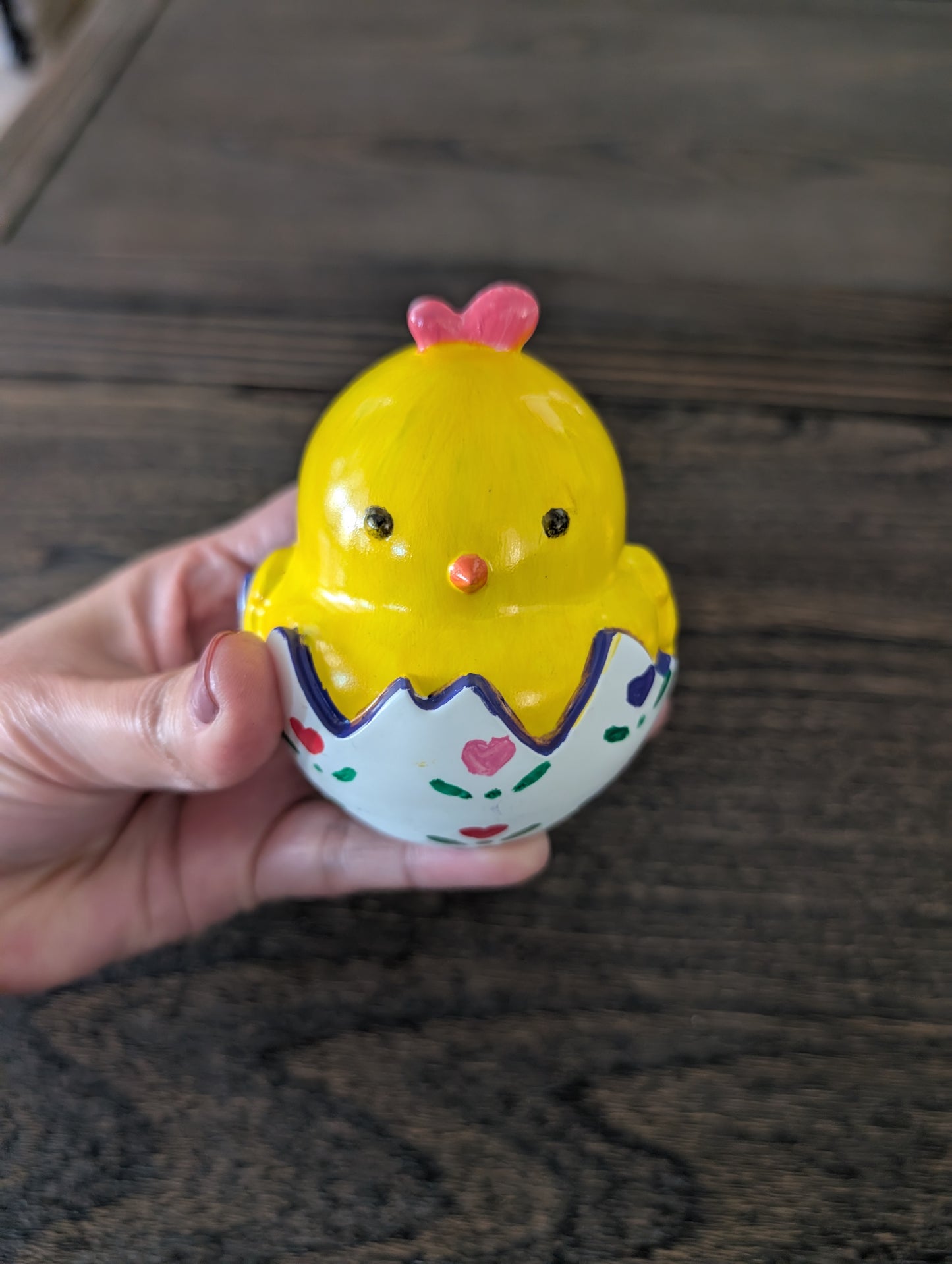 Yellow chick trinket in an egg held by a hand on a wooden surface