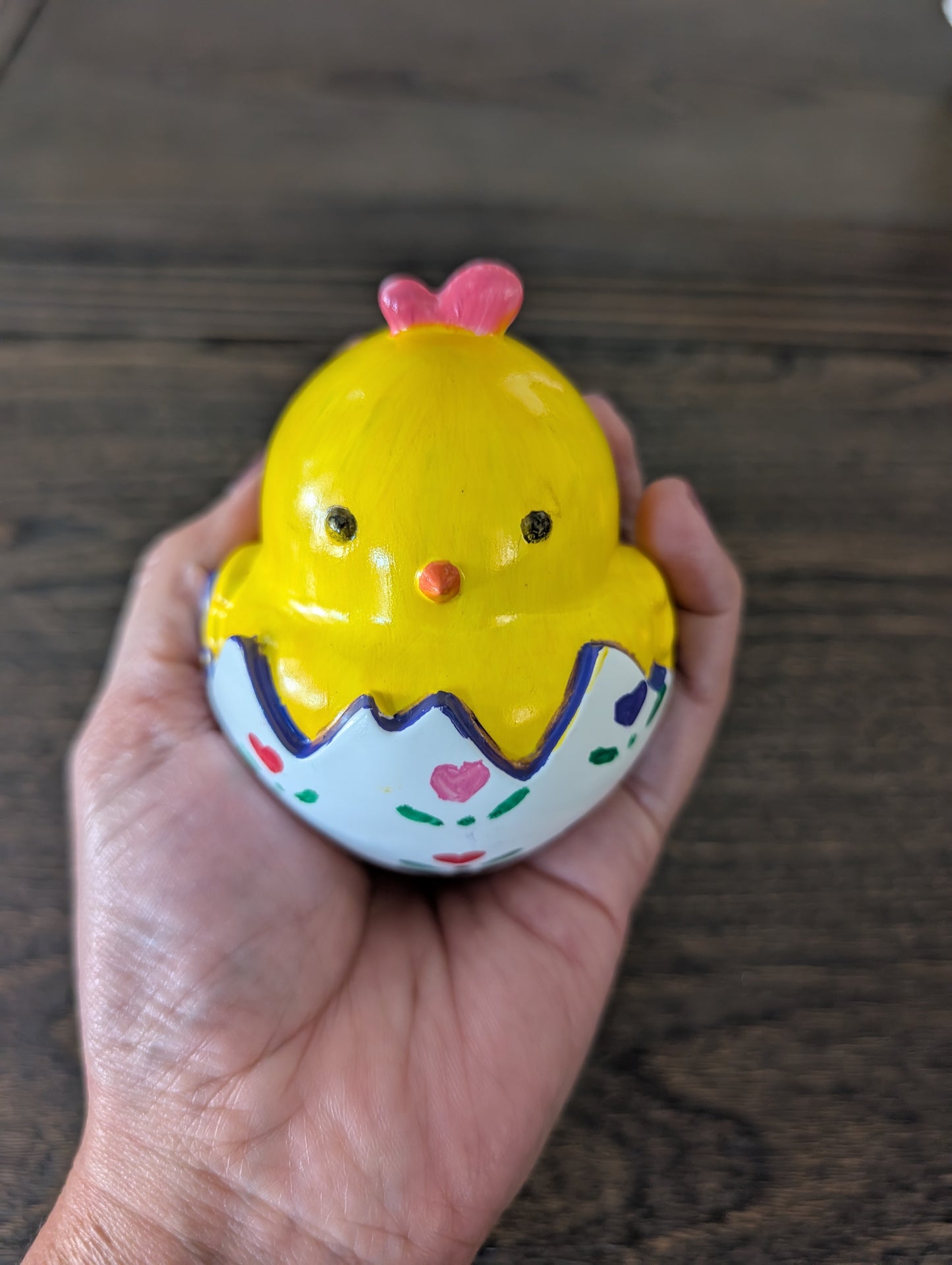Yellow chick trinket with a pink bow held in a hand on a wooden surface