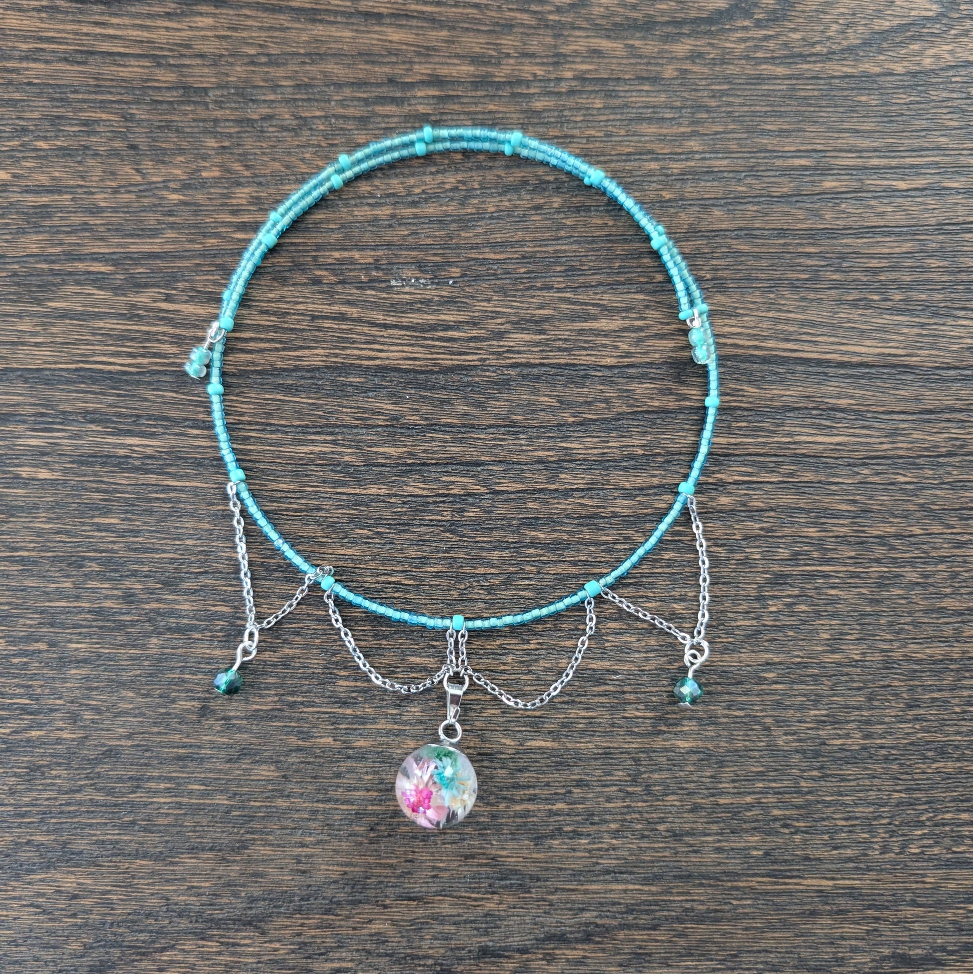 Turquoise beaded necklace with a small round charm on a wooden surface