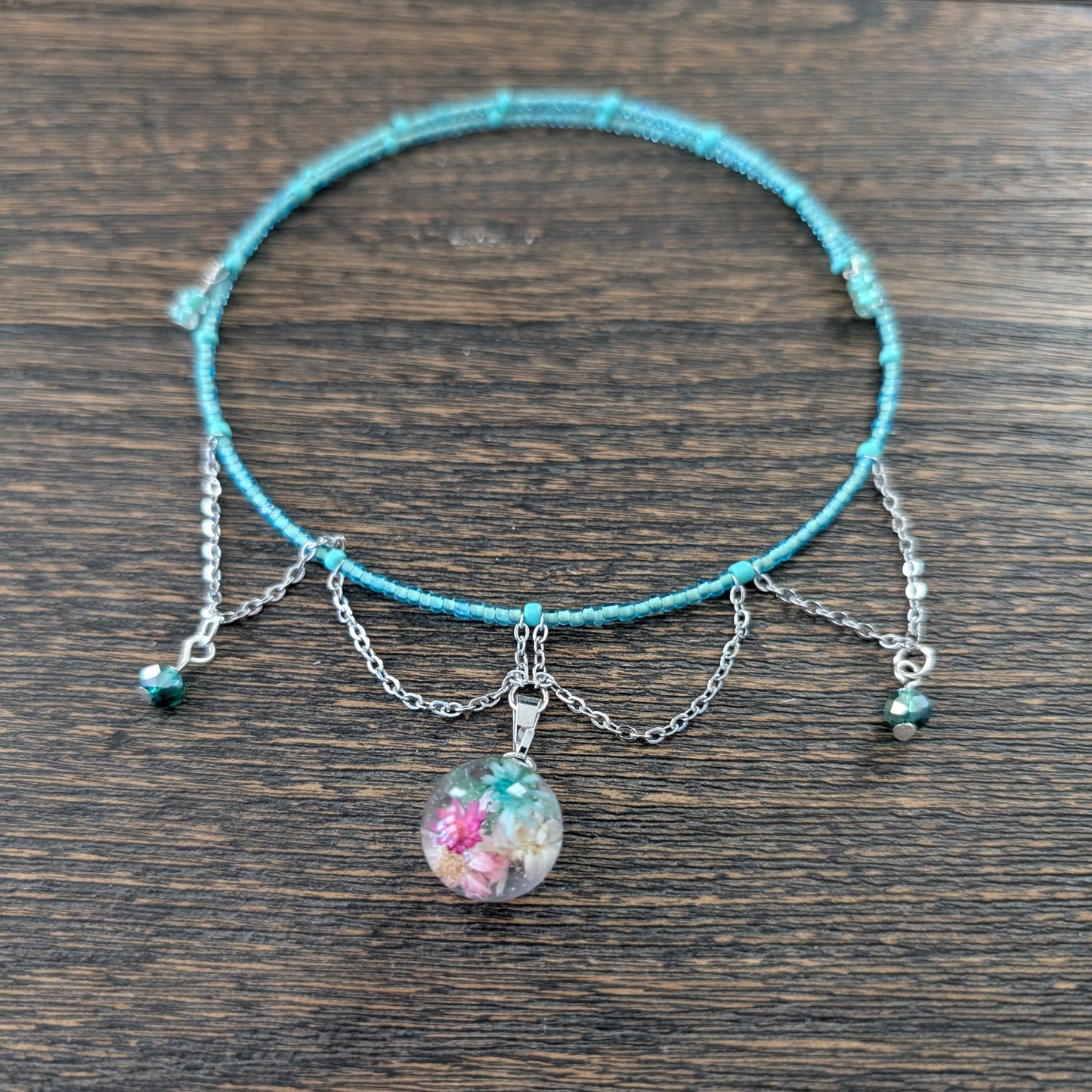 Turquoise necklace with a silver chain and floral charm on a wooden surface