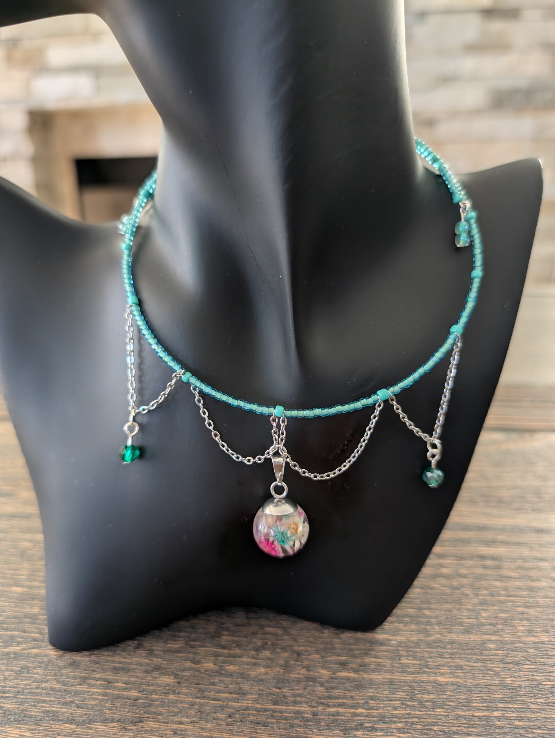 Turquoise beaded necklace with charms on a black mannequin bust.