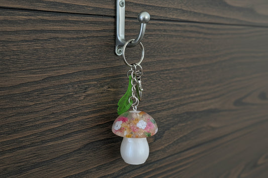 Mushroom-shaped keychain with floral design held by a hand on a wooden surface