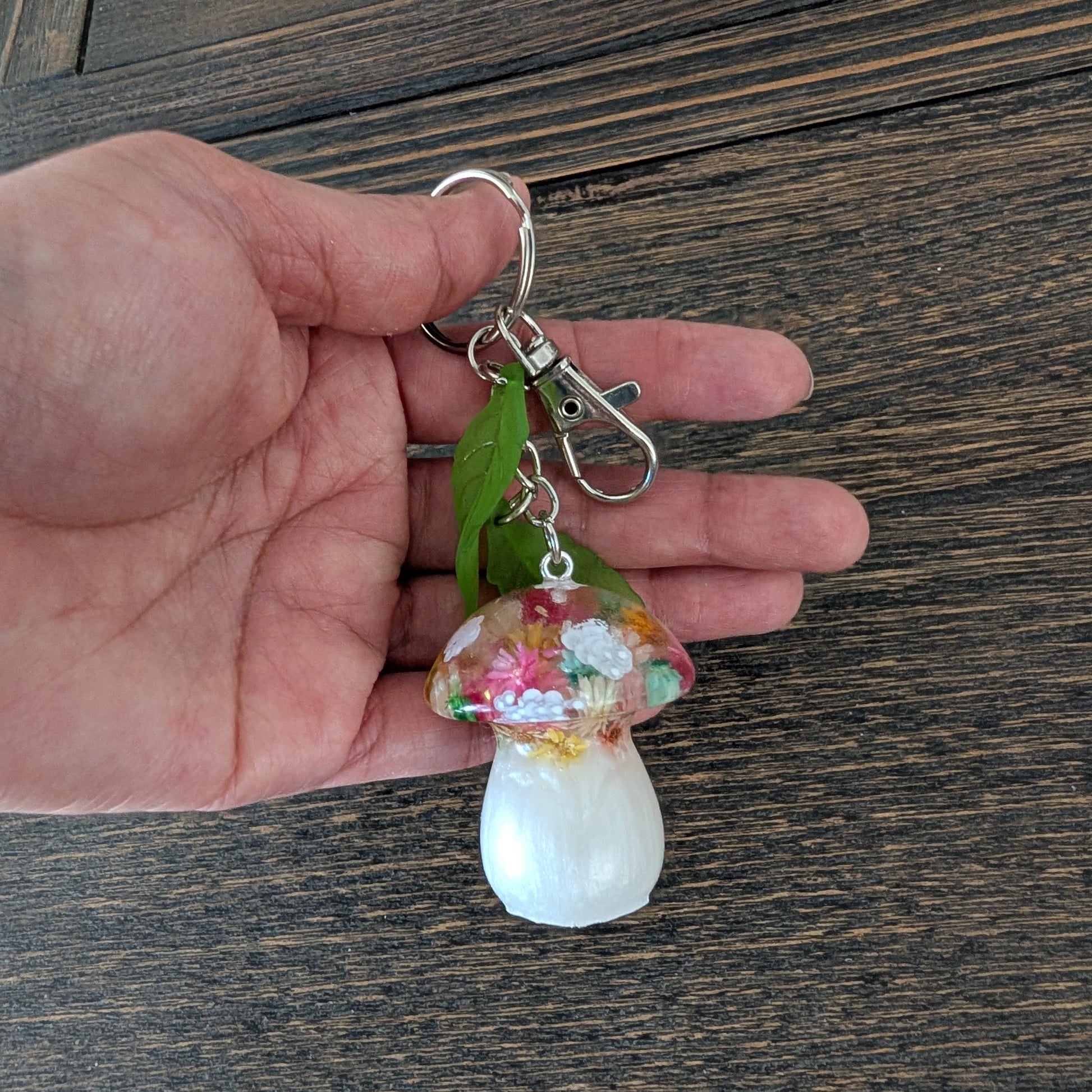 Hand holding a decorative mushroom keychain on a wooden surface