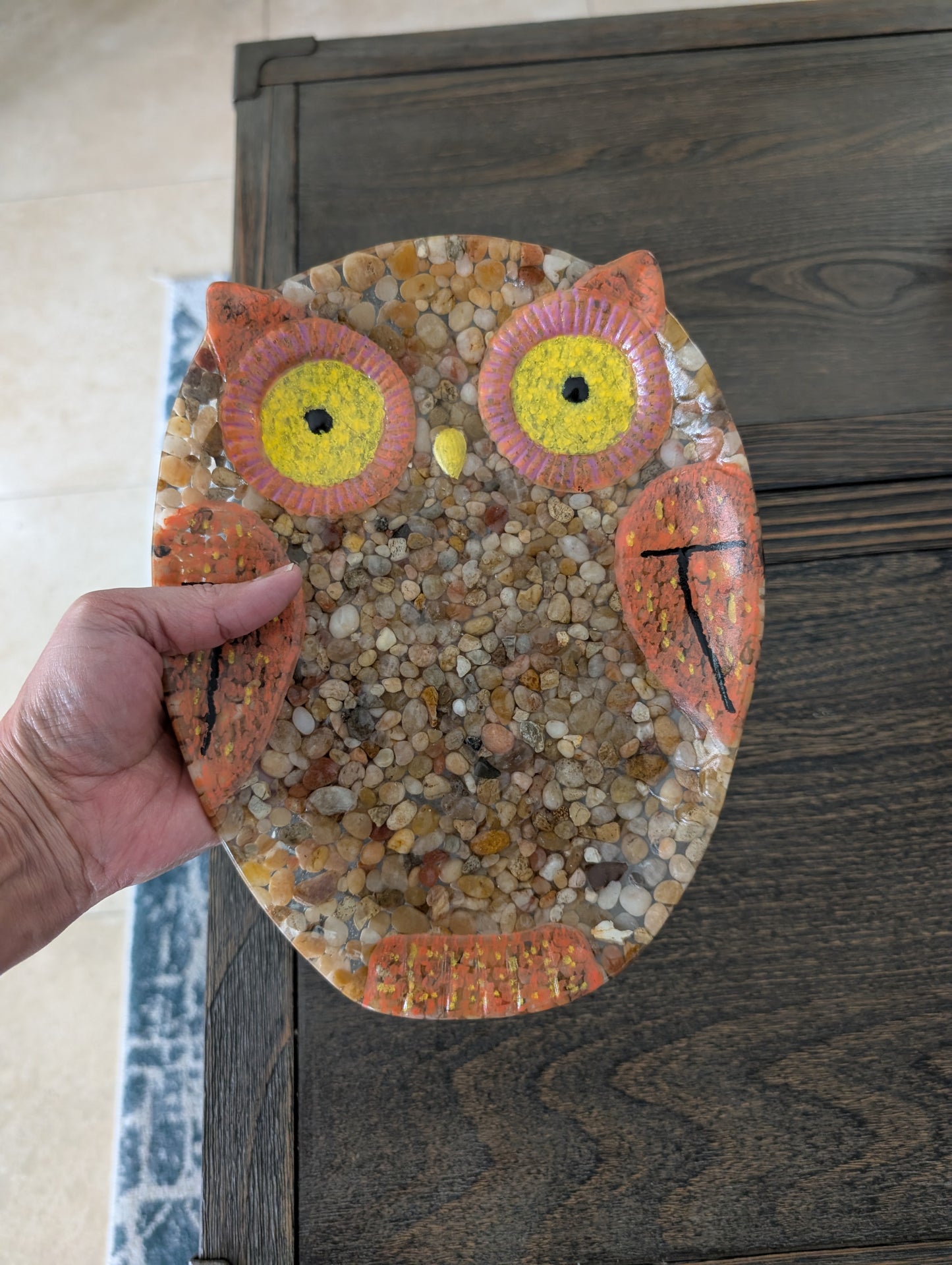 Hand holding a resin owl art piece against a wooden background