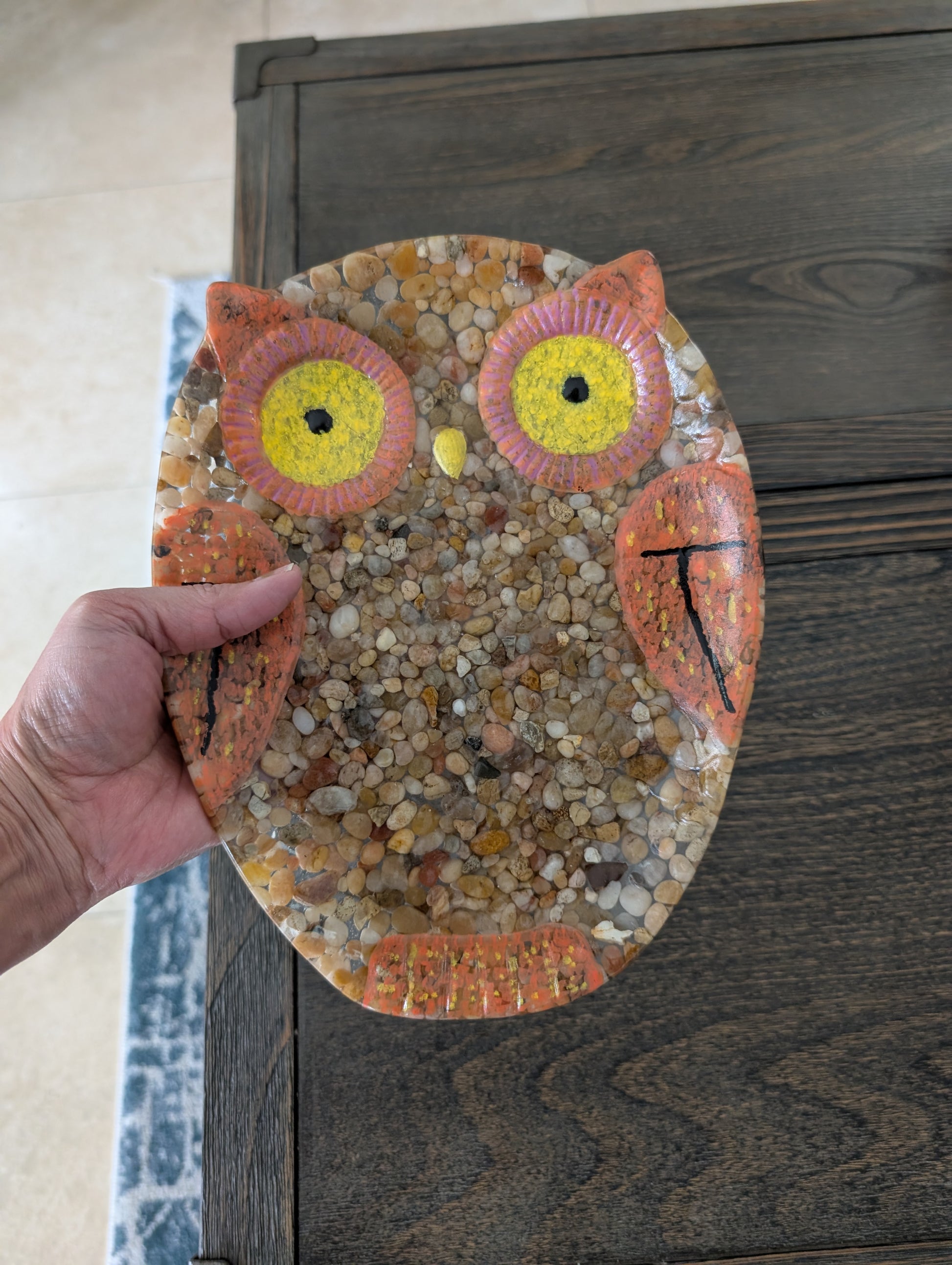 Hand holding a resin owl art piece against a wooden background