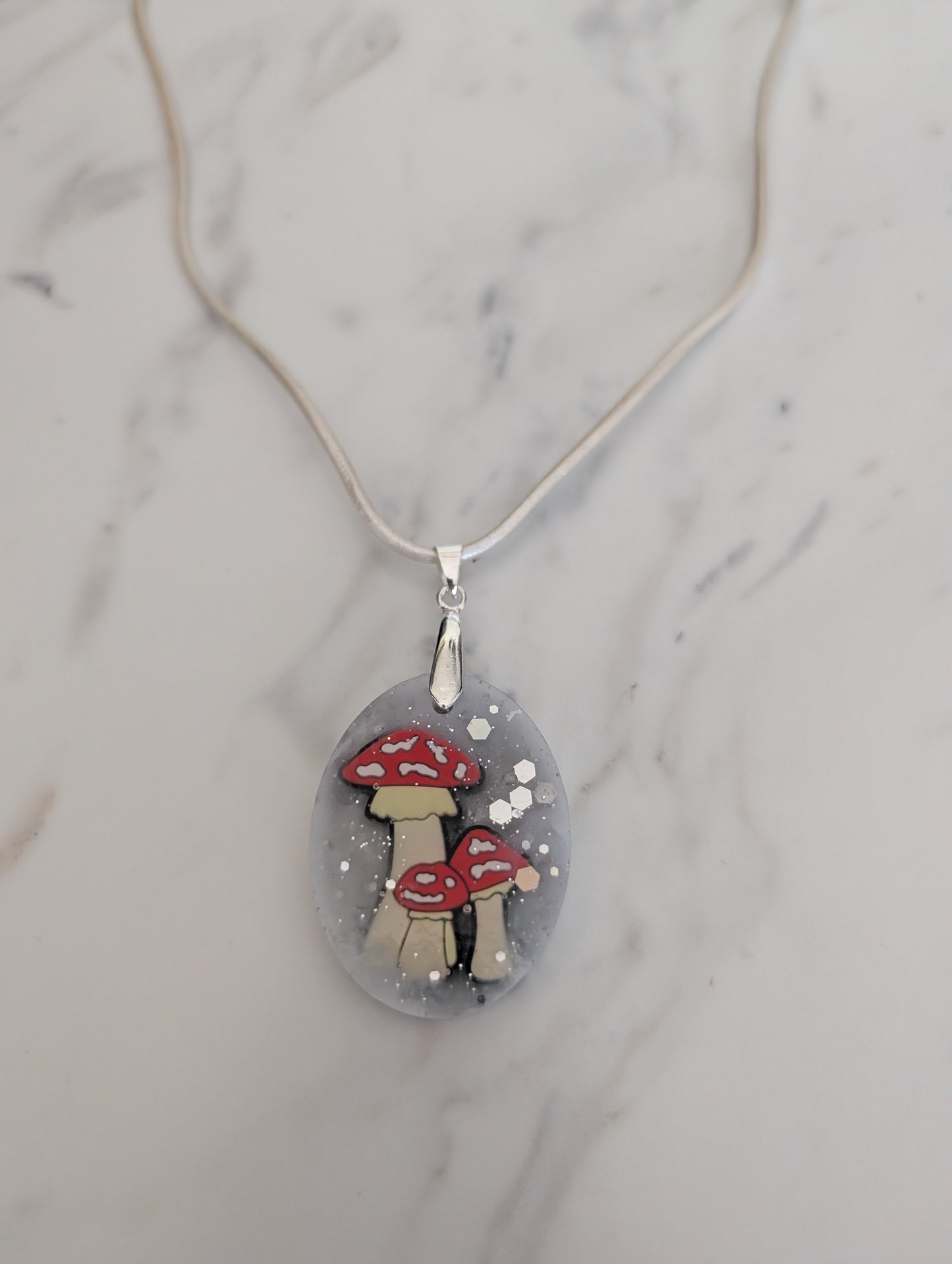 Necklace with a pendant featuring red and white mushroom design on a marble surface