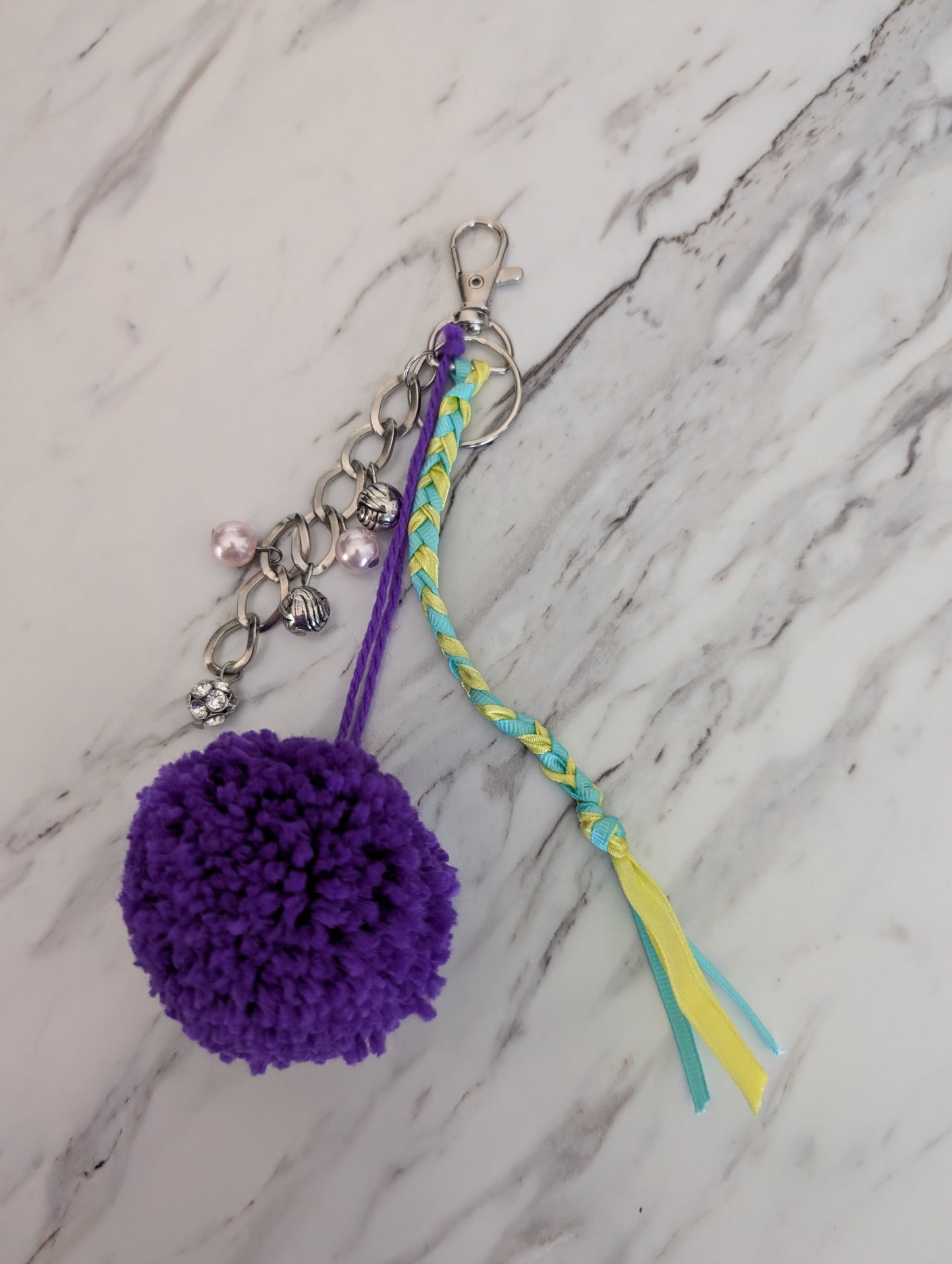 Purple pom-pom keychain with braided string and tassel on a marble surface