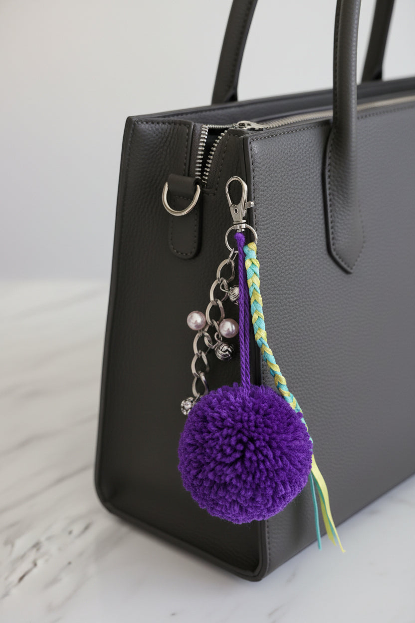 Purple pom-pom keychain with braided string and beaded chain on a black bag
