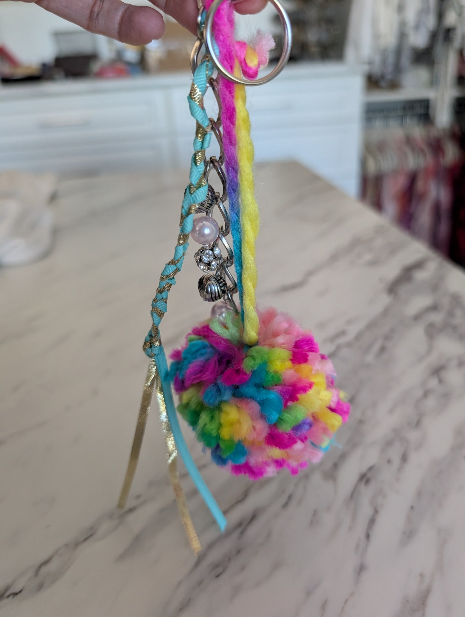 Colorful pom-pom keychain with beads on a marble surface
