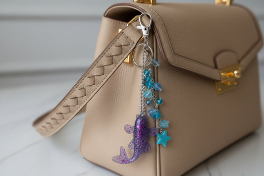 Beige handbag with a decorative keychain featuring a purple fish and blue beads.