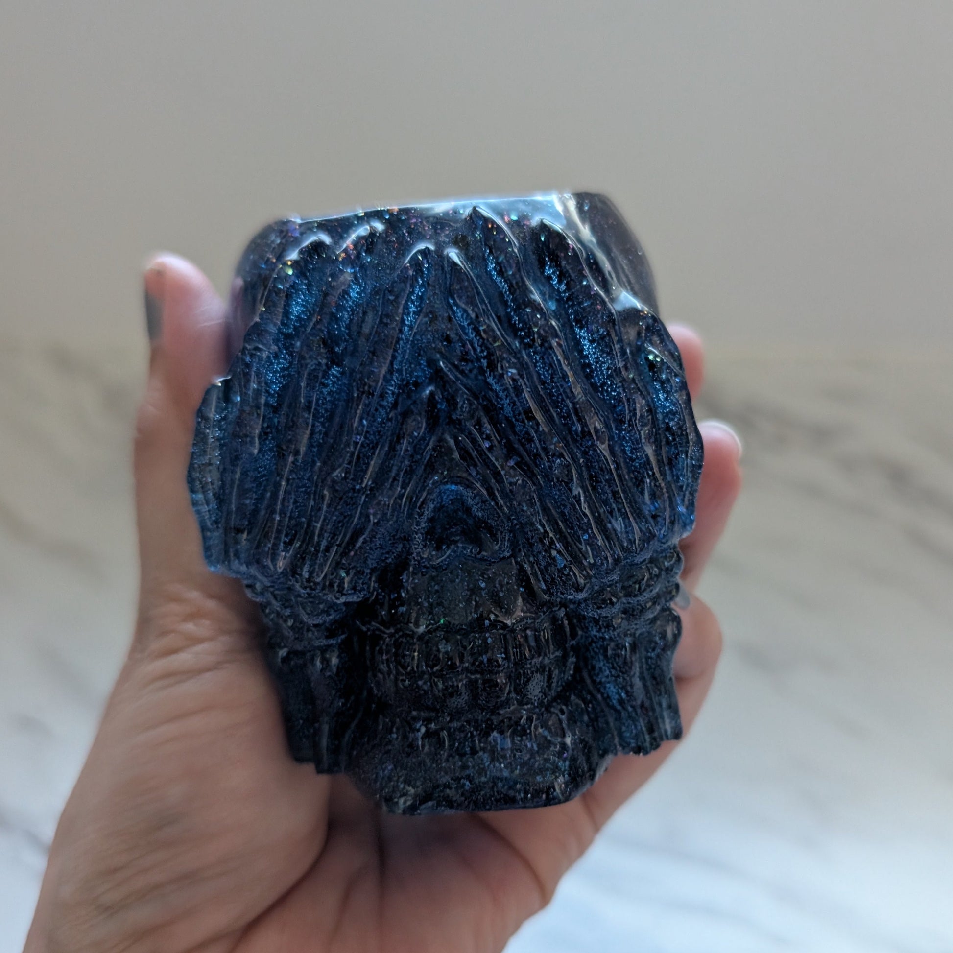 Hand holding a dark blue see no Evil Skull trinket holder against a neutral background