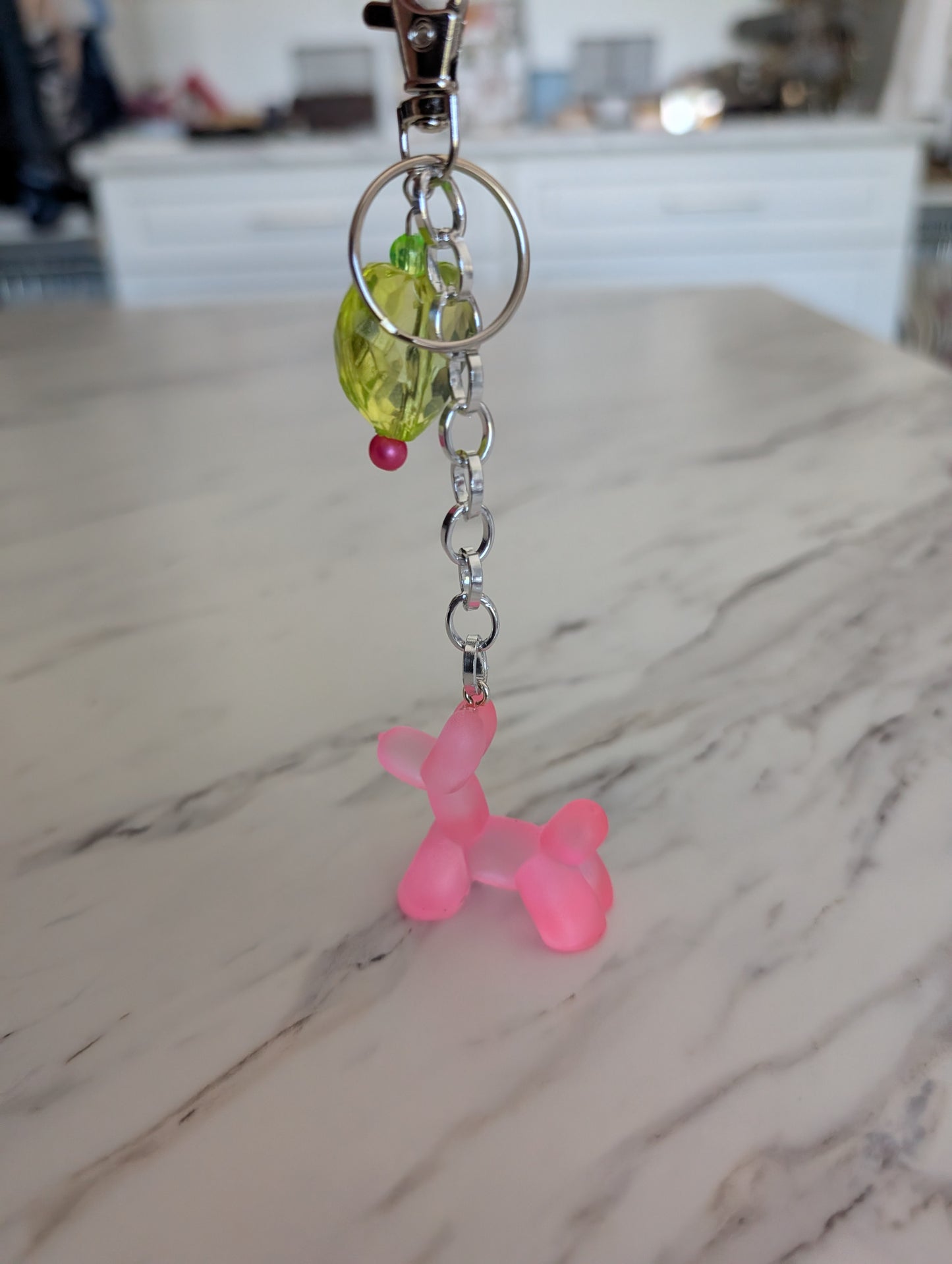 Keychain with pink balloon dog charm and green heart-shaped charm on a marble surface