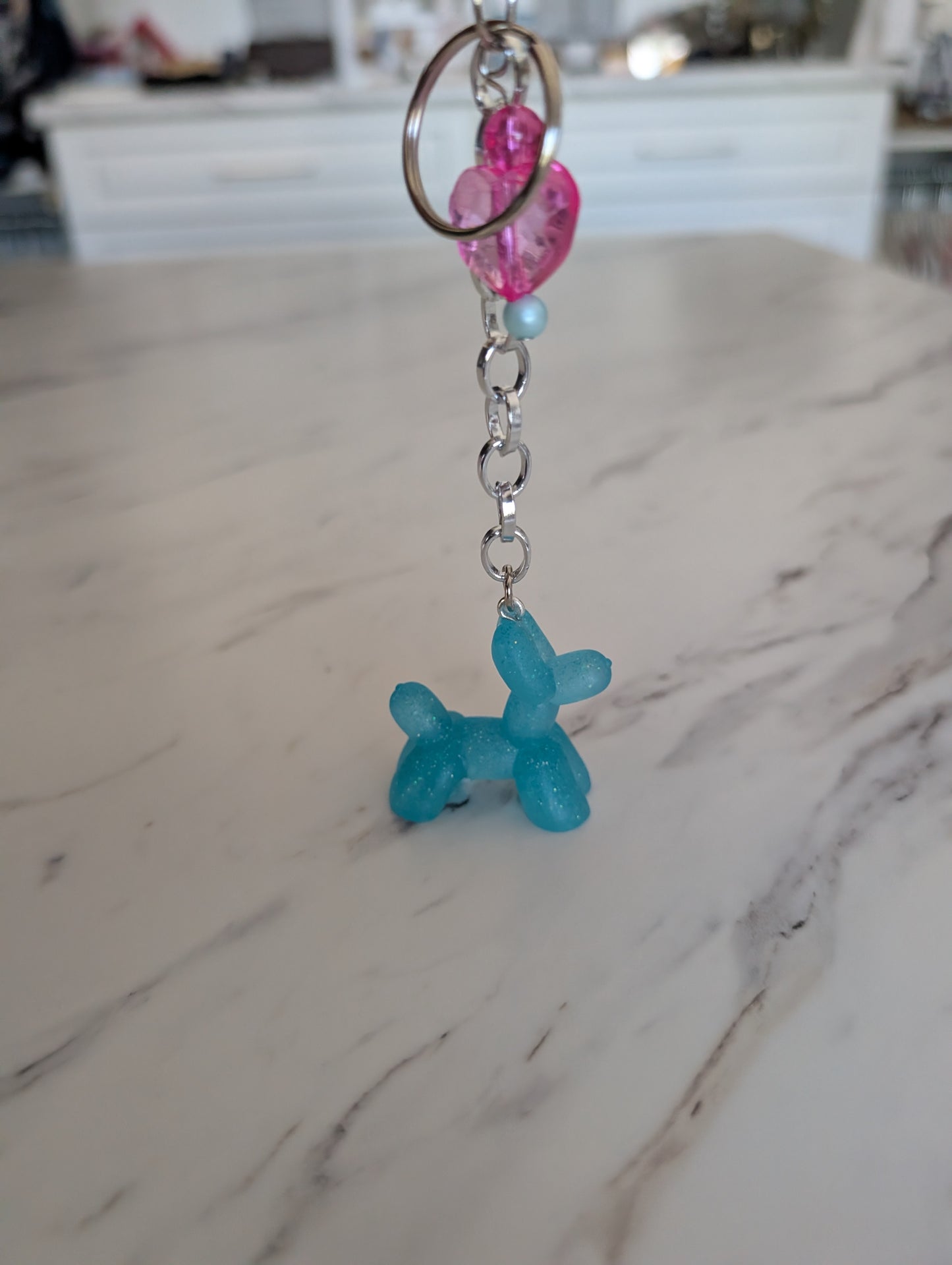 Blue balloon dog keychain with pink and blue beads on a marble surface