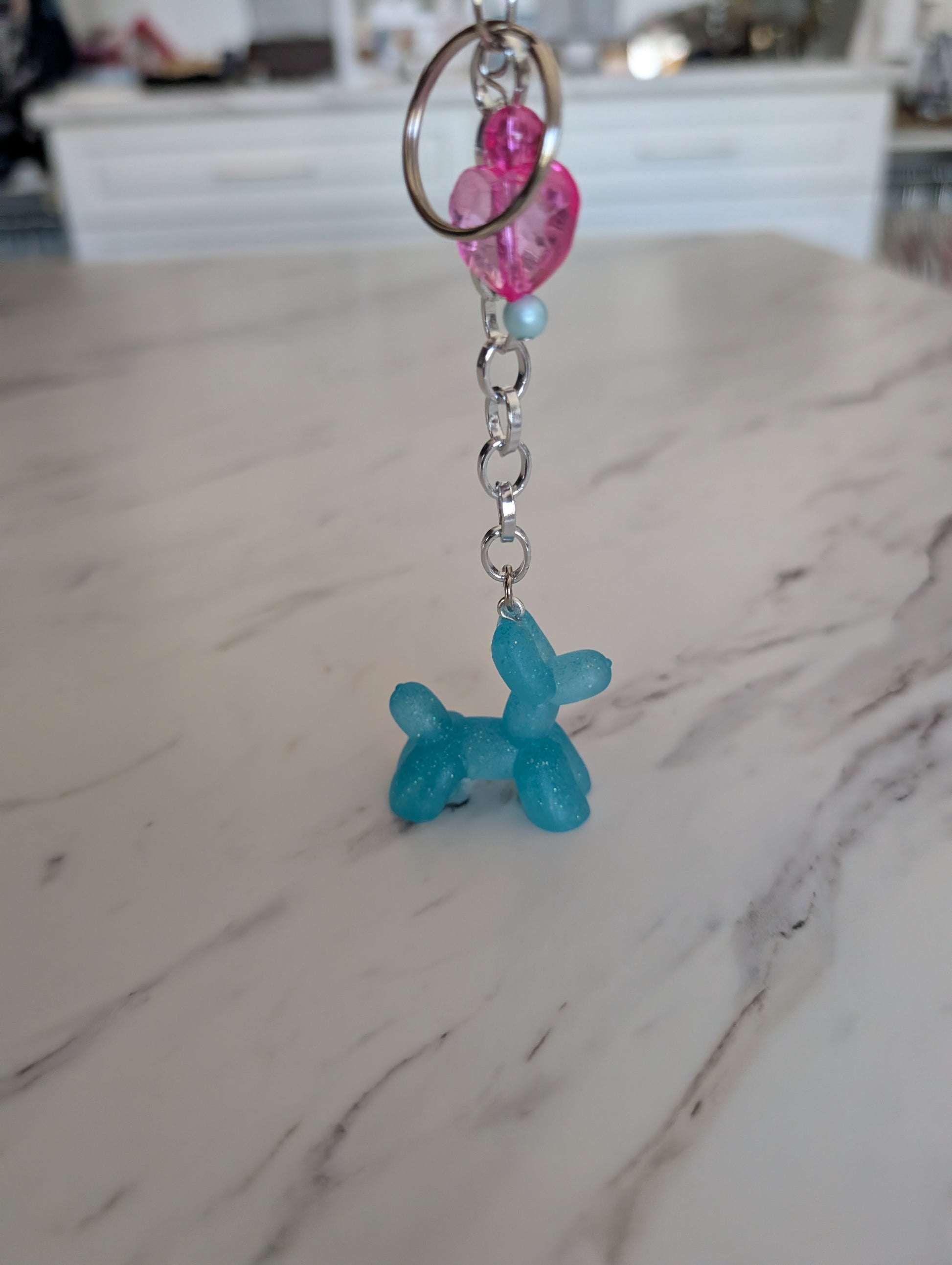 Blue balloon dog keychain with pink and blue beads on a marble surface