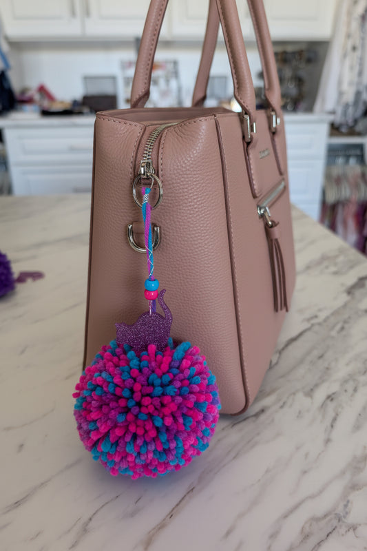 Colorful pom-pom with cat charm keychain on a marble surface with a blurred background
