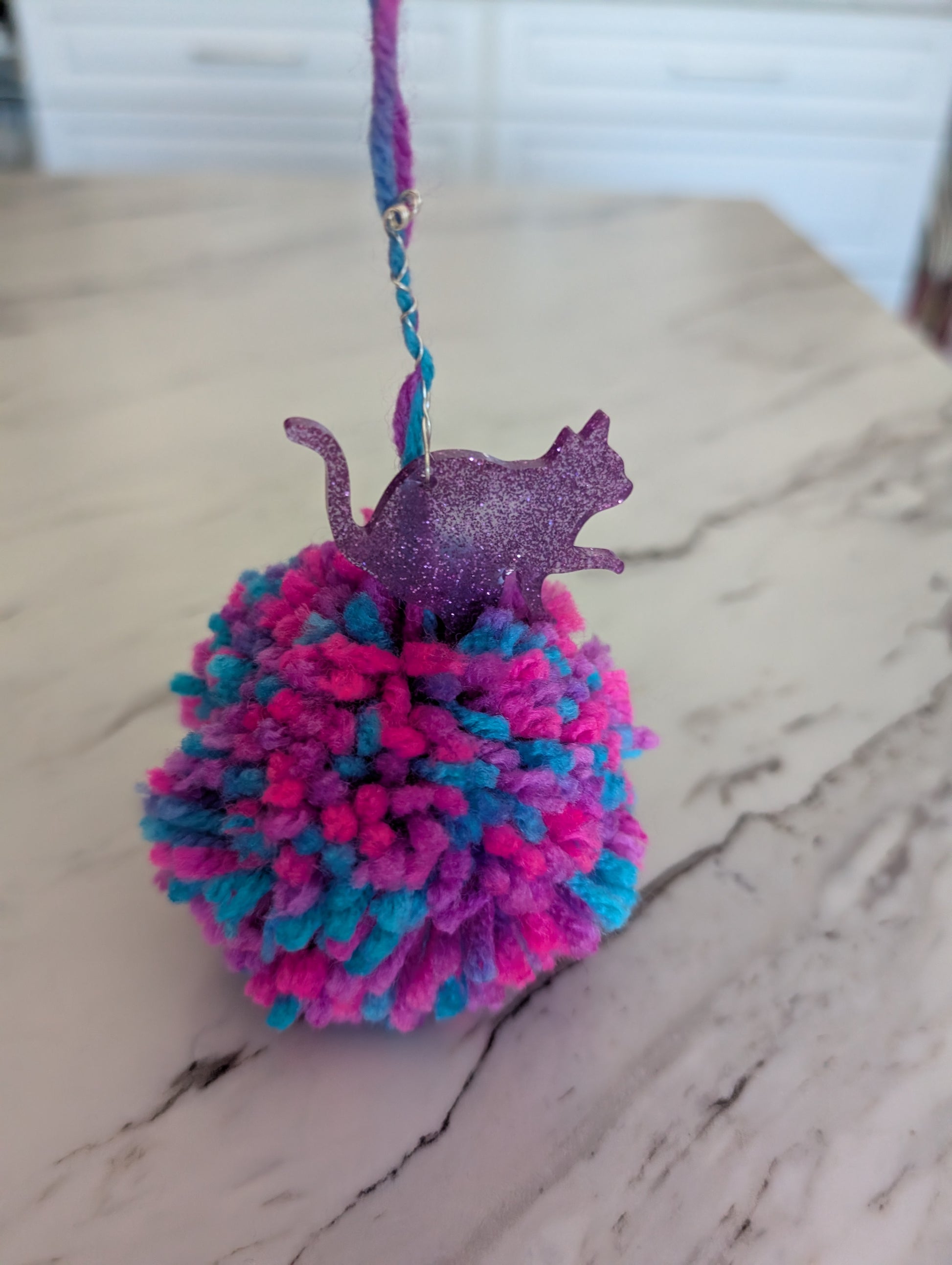 Multicolored pom-pom cat keychain on a marble surface.