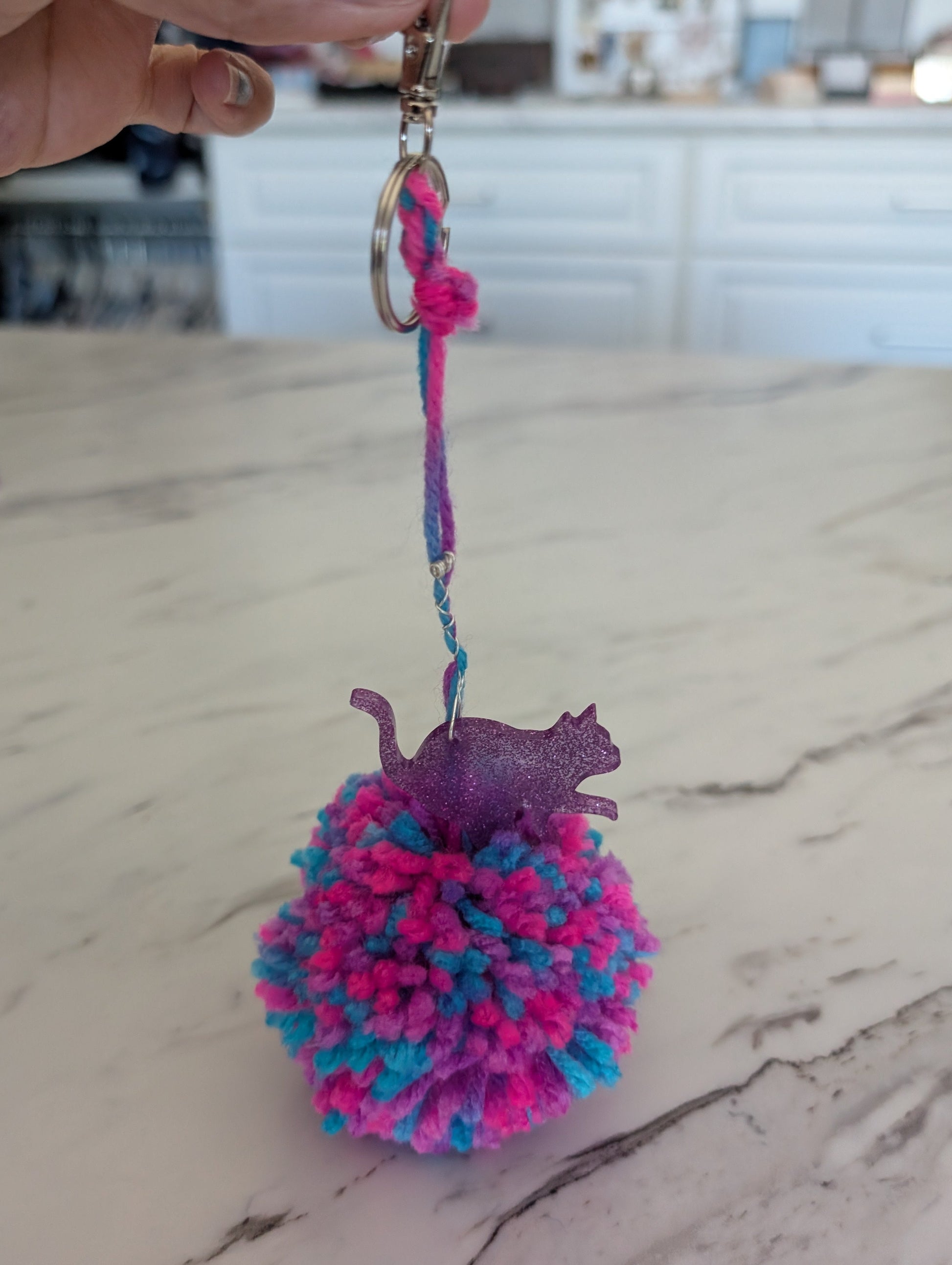 Colorful pom-pom keychain with a cat figure on a marble surface