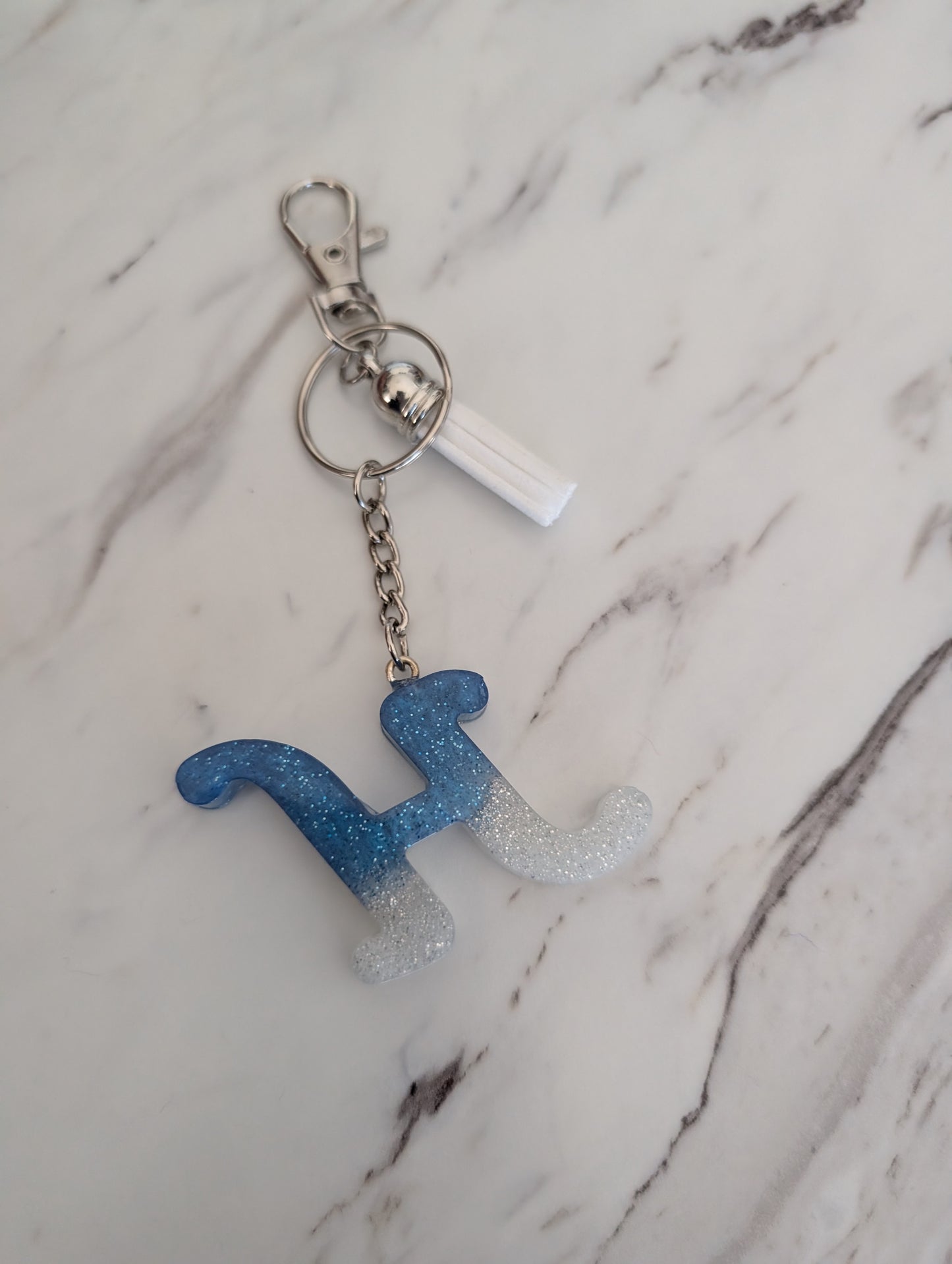 Blue glittery letter H keychain on a marble surface