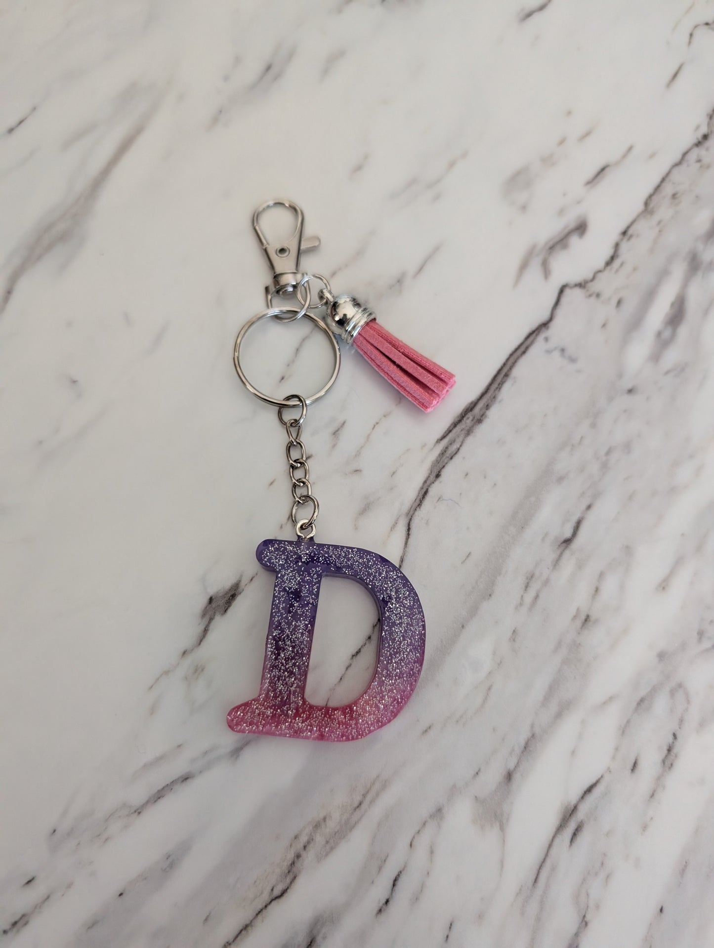 purple and pink Keychain with letter 'D' and pink tassel on a marble background