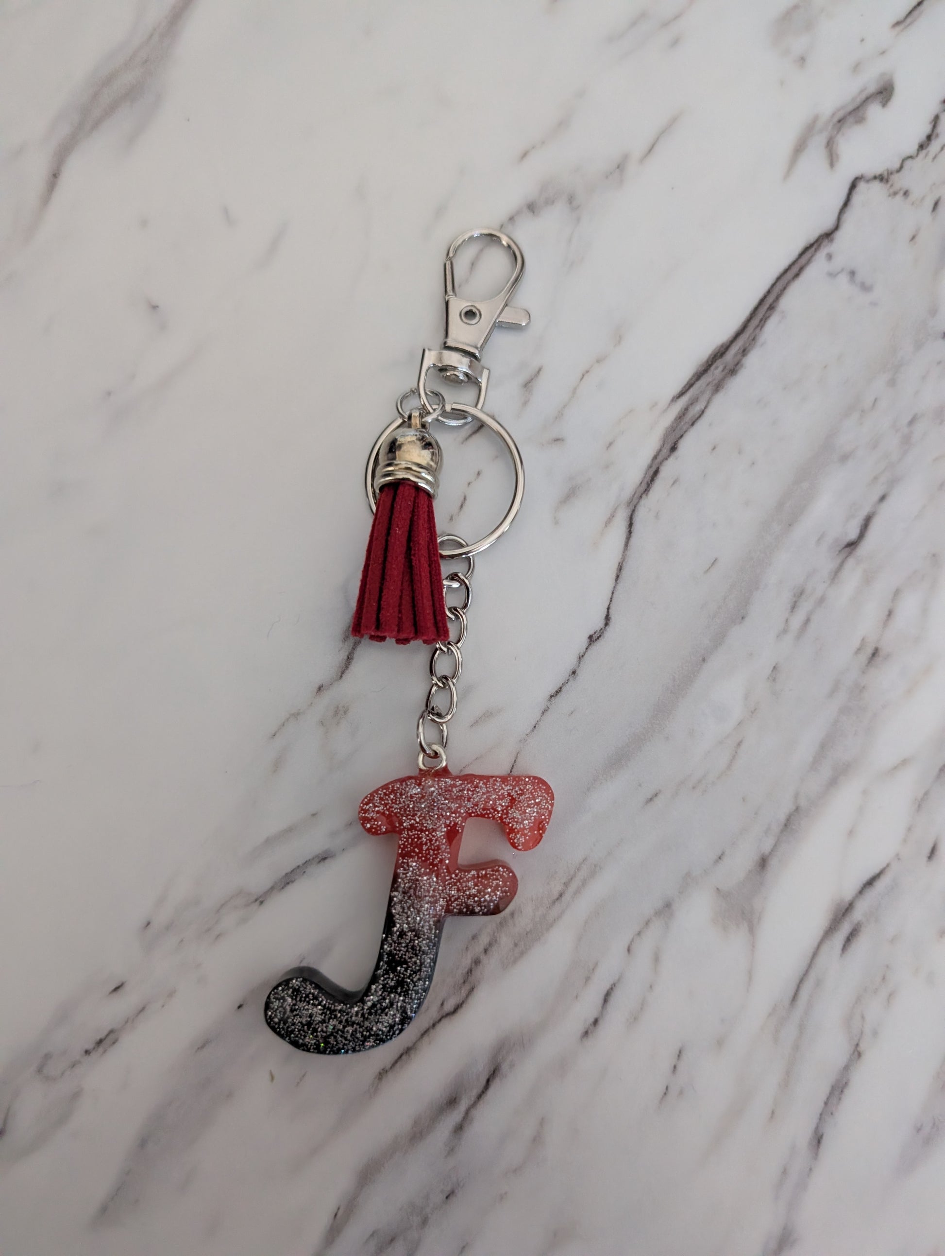 Keychain with letter 'F' and red tassel on a marble background